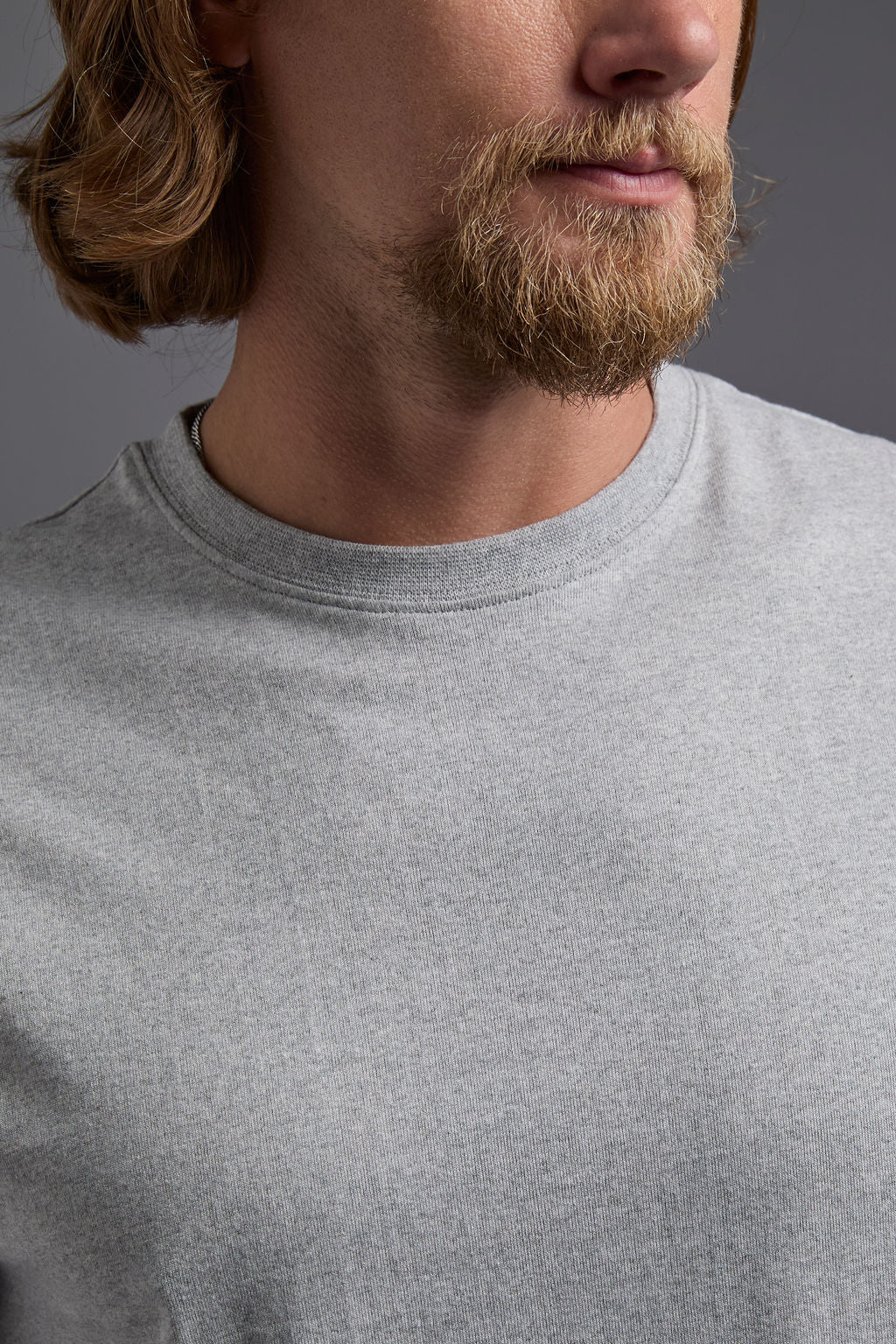 A blonde, male model with a beard wearing the men's core renewal tee in the color light grey melange heather and black Levi 501® jeans from a front collar view on a gray background. The core renewal tee is made out of a sustainable blend of repurposed recycled garments: 60% recycled cotton and 40% recycled polyester. #light-grey-melange