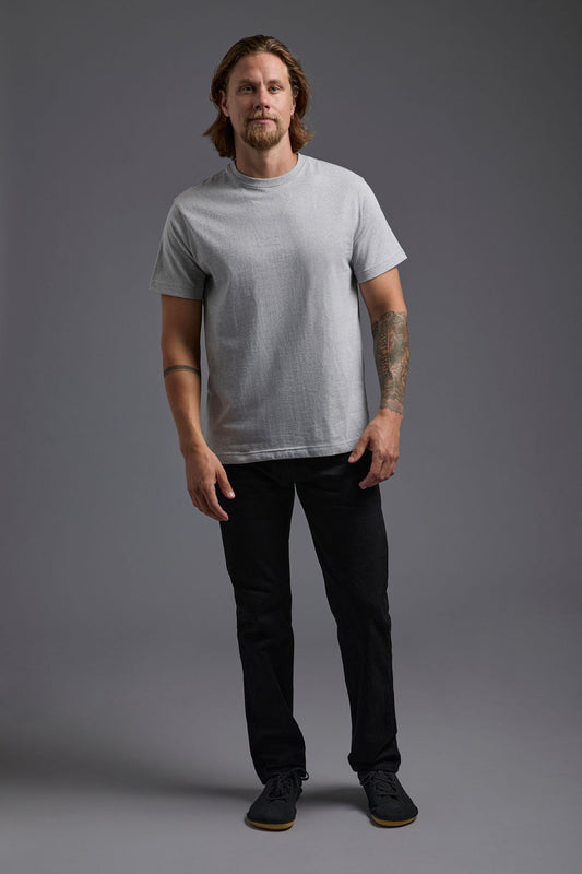 A blonde, male model with a beard wearing the men's core renewal tee in the color light grey melange heather and black Levi 501® jeans from a front view on a gray background. The core renewal tee is made out of a sustainable blend of repurposed recycled garments: 60% recycled cotton and 40% recycled polyester. #light-grey-melange