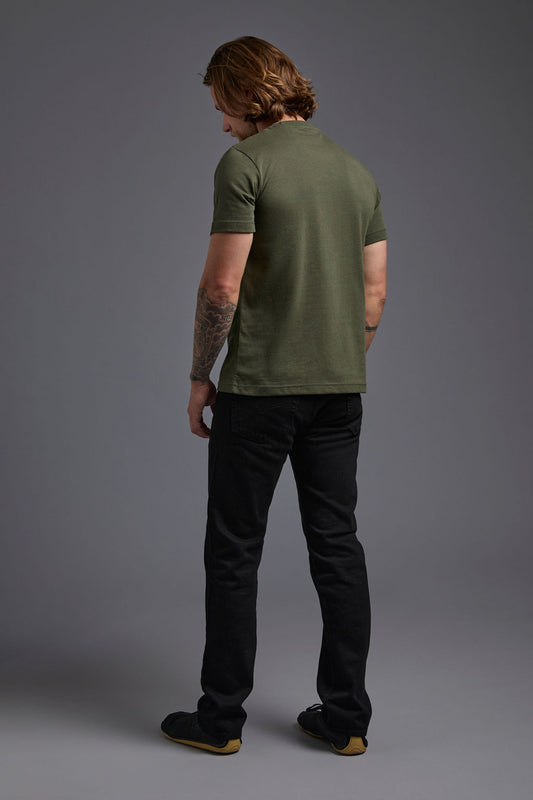 A blonde, male model with a beard wearing the men's core renewal tee in the color military green and black Levi 501® jeans from a back view on a gray background. The core renewal tee is made out of a sustainable blend of repurposed recycled garments: 60% recycled cotton and 40% recycled polyester. #military-green