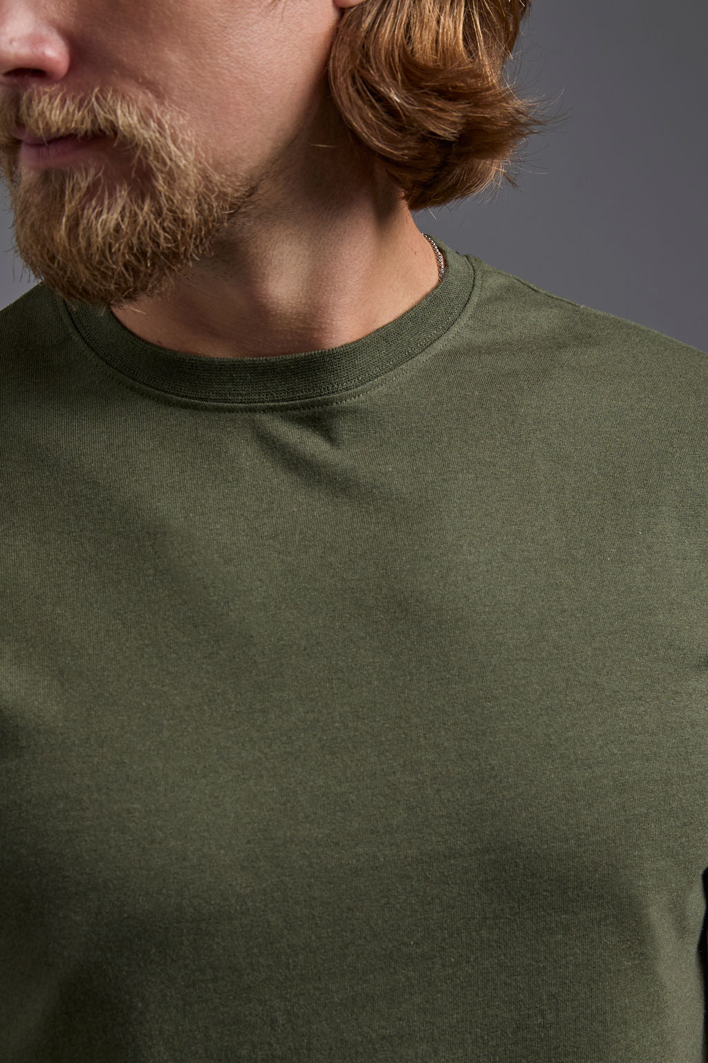 A blonde, male model with a beard wearing the men's core renewal tee in the color military green and black Levi 501® jeans from a front close up collar view on a gray background. The core renewal tee is made out of a sustainable blend of repurposed recycled garments: 60% recycled cotton and 40% recycled polyester. #military-green
