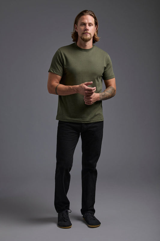 A blonde, male model with a beard wearing the men's core renewal tee in the color military green and black Levi 501® jeans from a front view on a gray background. The core renewal tee is made out of a sustainable blend of repurposed recycled garments: 60% recycled cotton and 40% recycled polyester. #military-green