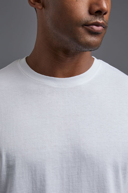 An African American male model with a beard wearing the men's core renewal tee in the color white and forest cargo pants from a front close up view on a gray background. The core renewal tee is made out of a sustainable blend of repurposed recycled garments: 60% recycled cotton and 40% recycled polyester. #white
