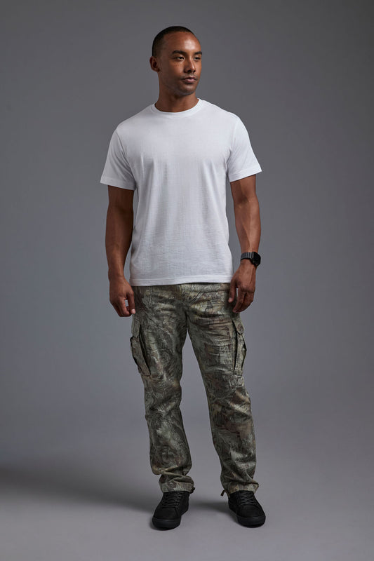 An African American male model with a beard wearing the men's core renewal tee in the color white and forest cargo pants from a front view on a gray background. The core renewal tee is made out of a sustainable blend of repurposed recycled garments: 60% recycled cotton and 40% recycled polyester. #white