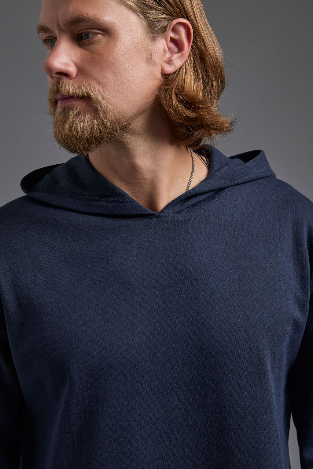 A blonde, male model with a beard on a gray background wearing the men's renewal hoodie in the color navy and black Levi 501® jeans. The renewal hoodie is made out of a sustainable blend of 60% recycled cotton and 40% recycled polyester, showing a relaxed fit from a close up collar view. #navy