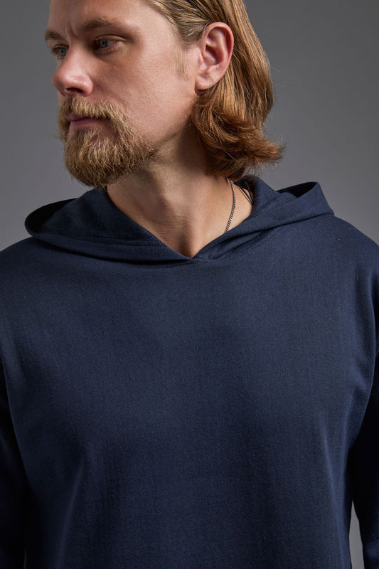 A blonde, male model with a beard on a gray background wearing the men's renewal hoodie in the color navy and black Levi 501® jeans. The renewal hoodie is made out of a sustainable blend of 60% recycled cotton and 40% recycled polyester, showing a relaxed fit from a close up collar view. #navy