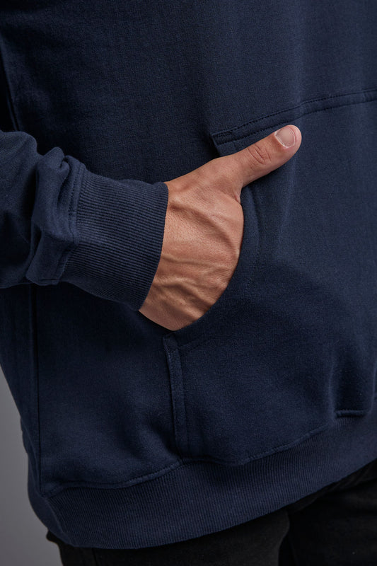 A blonde, male model with a beard on a gray background wearing the men's renewal hoodie in the color navy and black Levi 501® jeans. The renewal hoodie is made out of a sustainable blend of 60% recycled cotton and 40% recycled polyester, showing a close up kangaroo pocket view. #navy