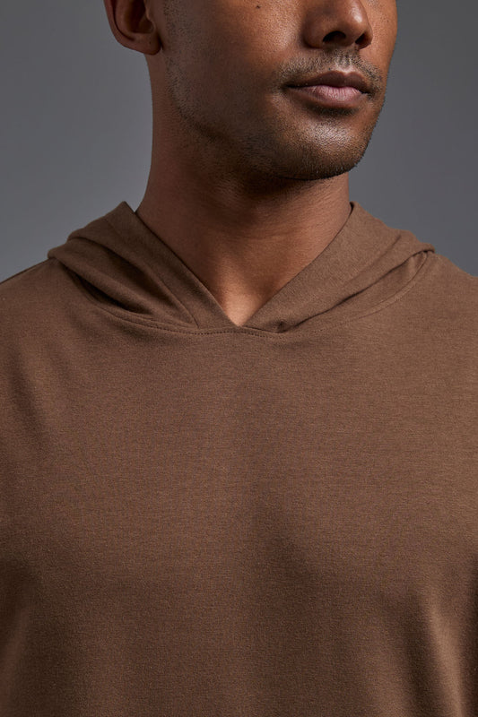 An African American male model on a gray background wearing the men's premium bamboo stretch hoodie in the color mocha brown, made out of 45% Bamboo, 50% Cotton, 5% Spandex, showing a relaxed fit from a front collar close up view. The model is wearing forest cargo pants and adidas sneakers. #mocha