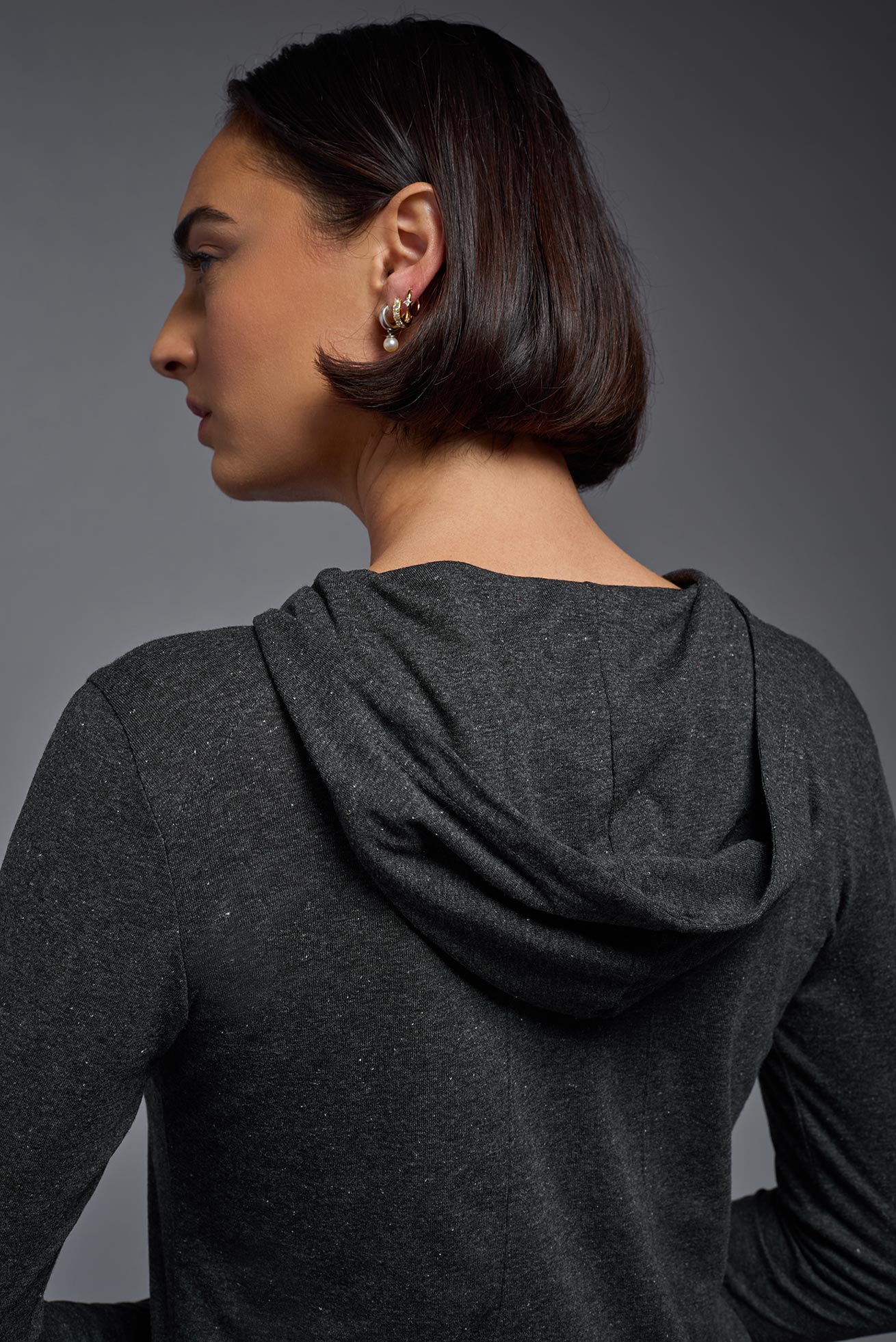 A female model wearing the women's Heather Hoodie Shirt in the color dark heather charcoal, made out of 88% polyester and 22% treated cotton, showing the relaxed fit from a back hoodie closeup view. This hoodie shirt is comfortable and made in the USA. #dark-heather-charcoal