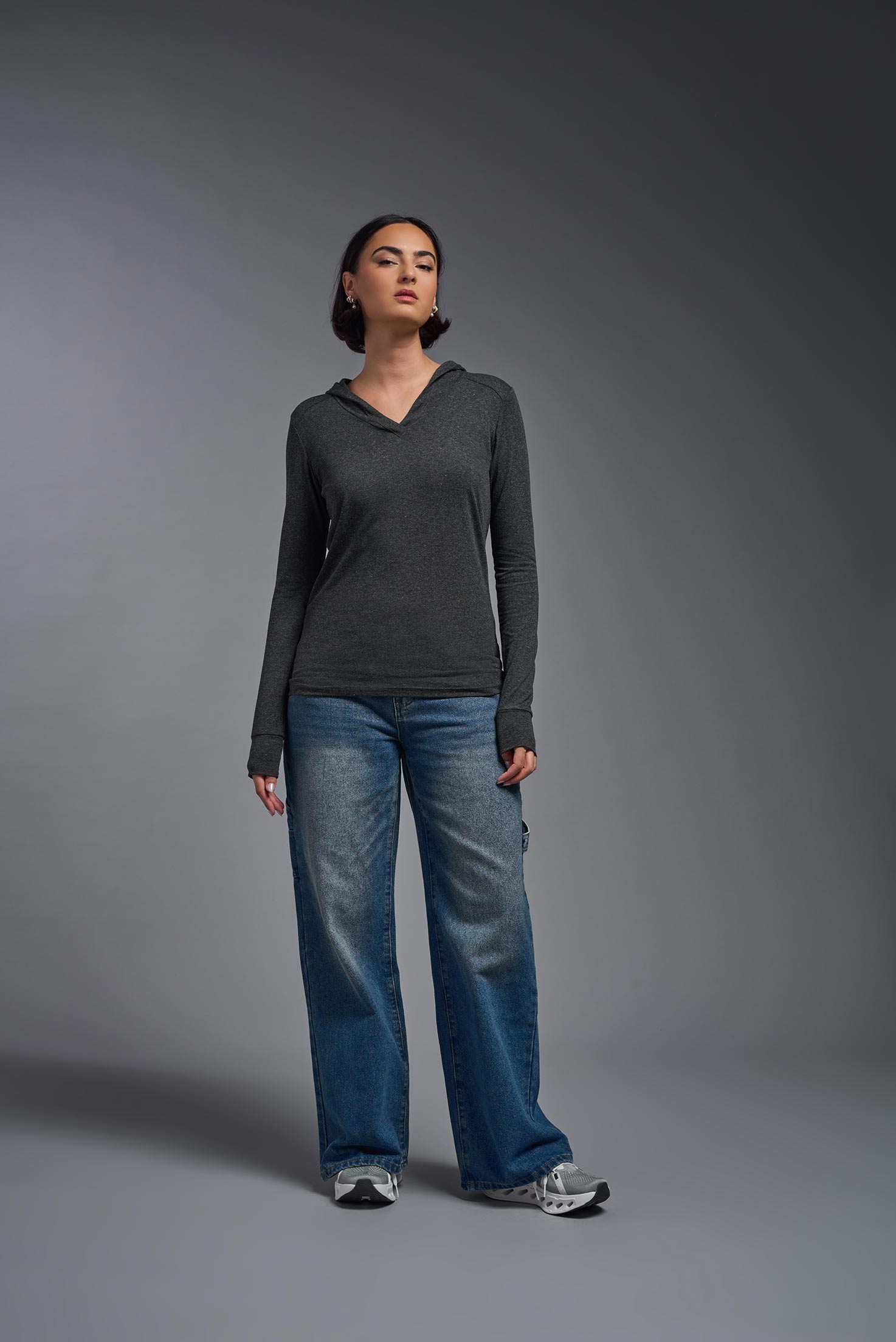 A female model wearing the women's Heather Hoodie Shirt in the color dark heather charcoal, made out of 88% polyester and 22% treated cotton, showing the relaxed fit from a front view. This hoodie shirt is comfortable and made in the USA. #dark-heather-charcoal