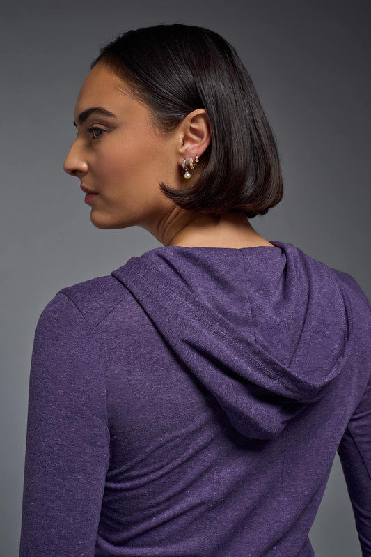A female model wearing the women's Heather Hoodie Shirt in the color dark purple heather, made out of 88% polyester and 22% treated cotton, showing the relaxed fit from a closeup back hoodie view. This hoodie shirt is comfortable and made in the USA. #dark-heather-purple
