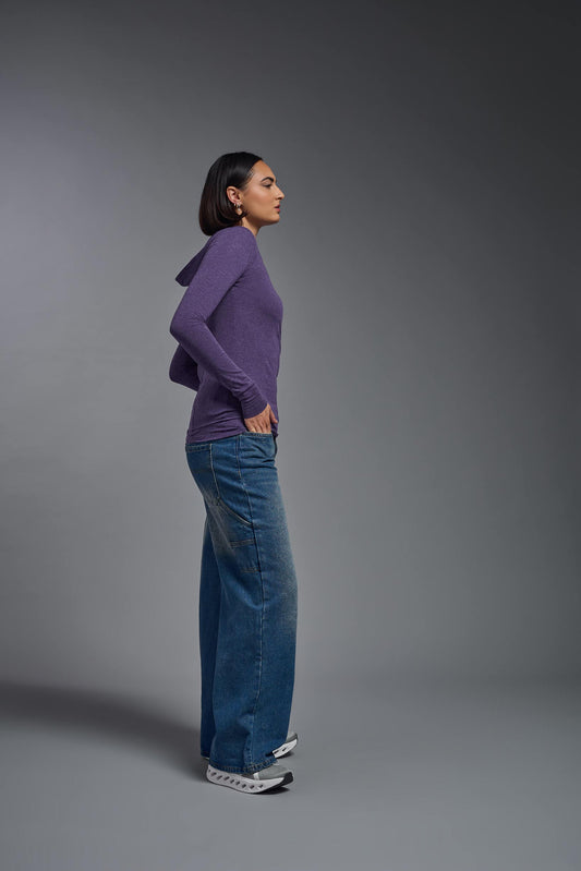 A female model wearing the women's Heather Hoodie Shirt in the color dark purple heather, made out of 88% polyester and 22% treated cotton, showing the relaxed fit from a side view. This hoodie shirt is comfortable and made in the USA. #dark-heather-purple