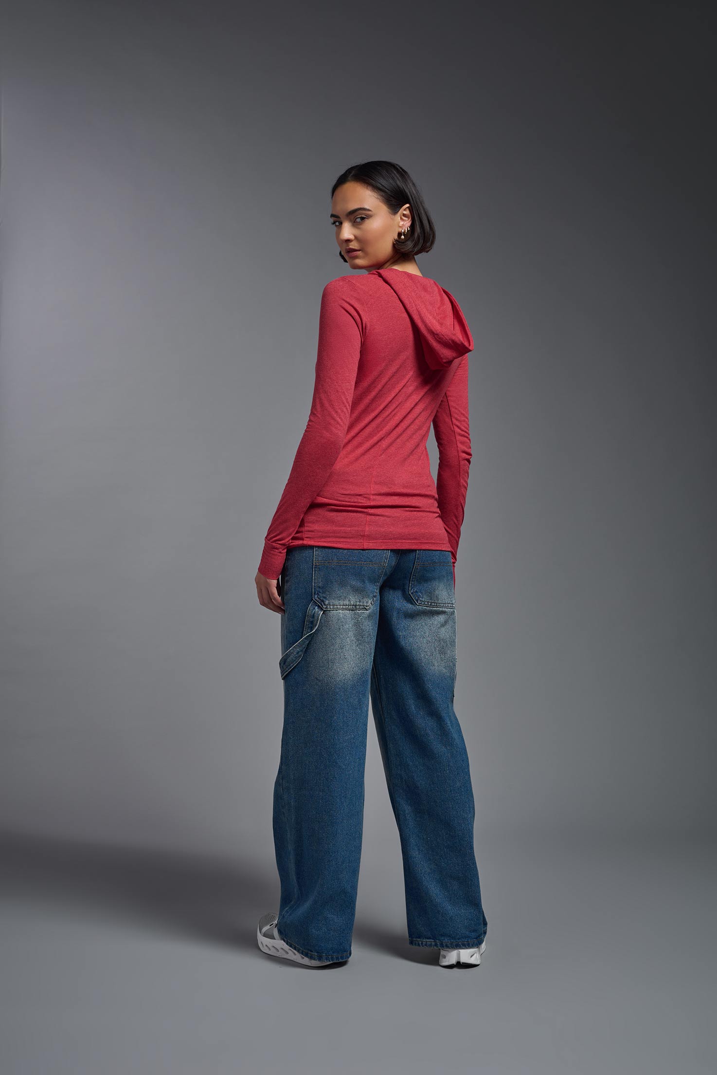 A female model wearing the women's Heather Hoodie Shirt in the color dark heather red, made out of 88% polyester and 22% treated cotton, showing the relaxed fit from a back view. This hoodie shirt is comfortable and made in the USA. #dark-heather-red