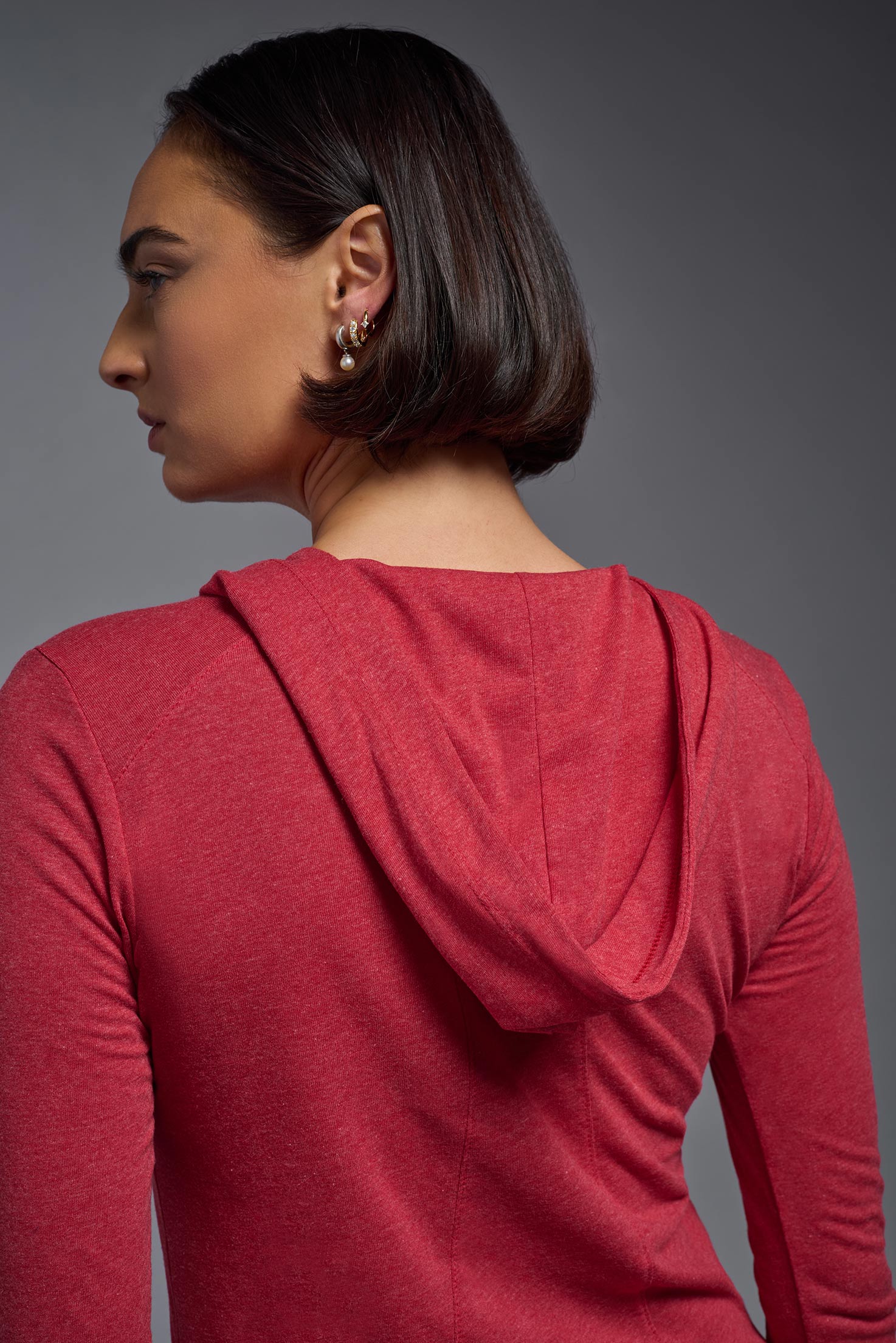A female model wearing the women's Heather Hoodie Shirt in the color dark heather red, made out of 88% polyester and 22% treated cotton, showing the relaxed fit from a closeup back hoodie view. This hoodie shirt is comfortable and made in the USA. #dark-heather-red