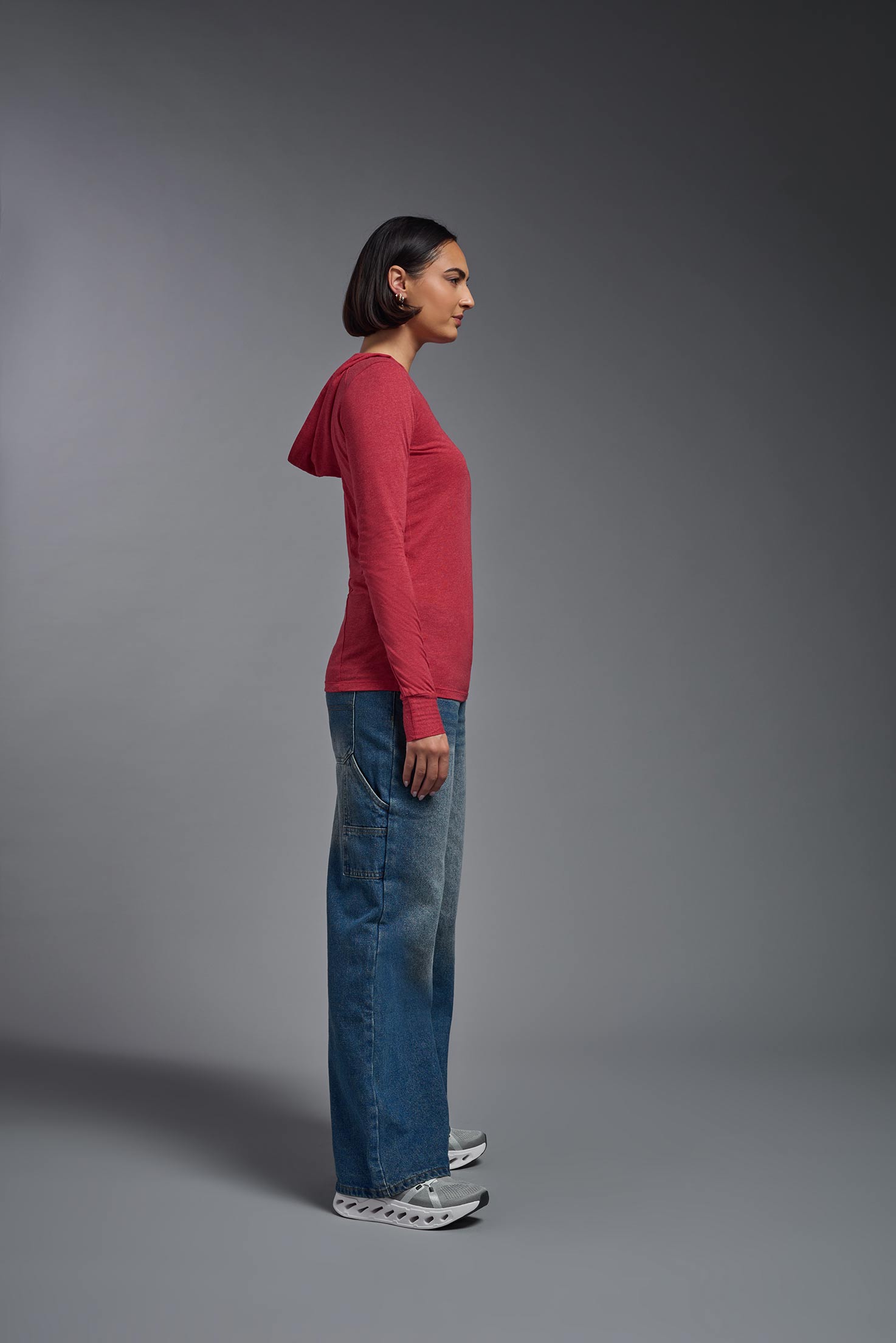 A female model wearing the women's Heather Hoodie Shirt in the color dark heather red, made out of 88% polyester and 22% treated cotton, showing the relaxed fit from a sideview. This hoodie shirt is comfortable and made in the USA. #dark-heather-red