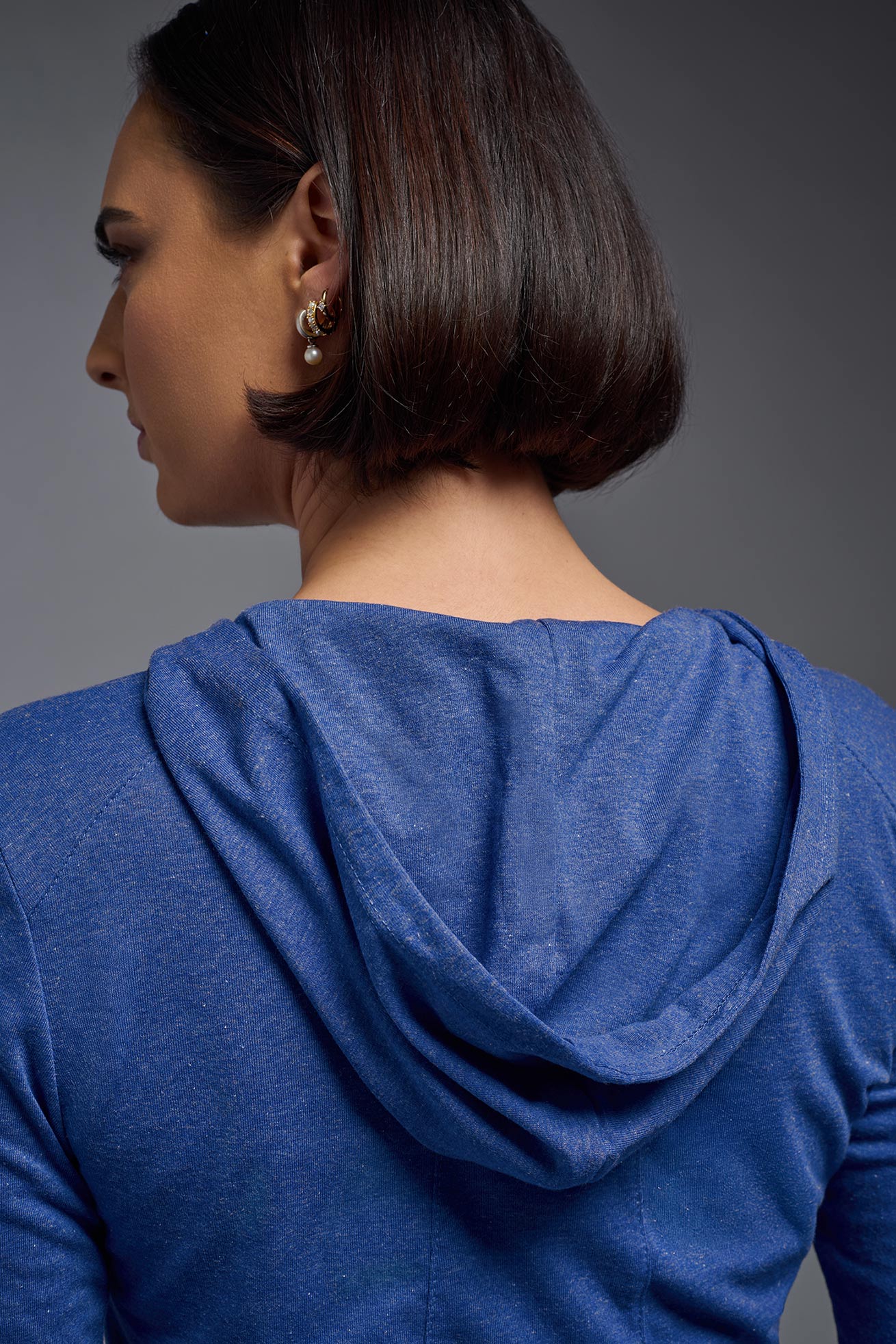 A female model wearing the women's Heather Hoodie Shirt in the color dark heather royal blue, made out of 88% polyester and 22% treated cotton, showing the relaxed fit from a back hoodie closeup view. This hoodie shirt is comfortable and made in the USA. #dark-heather-royal