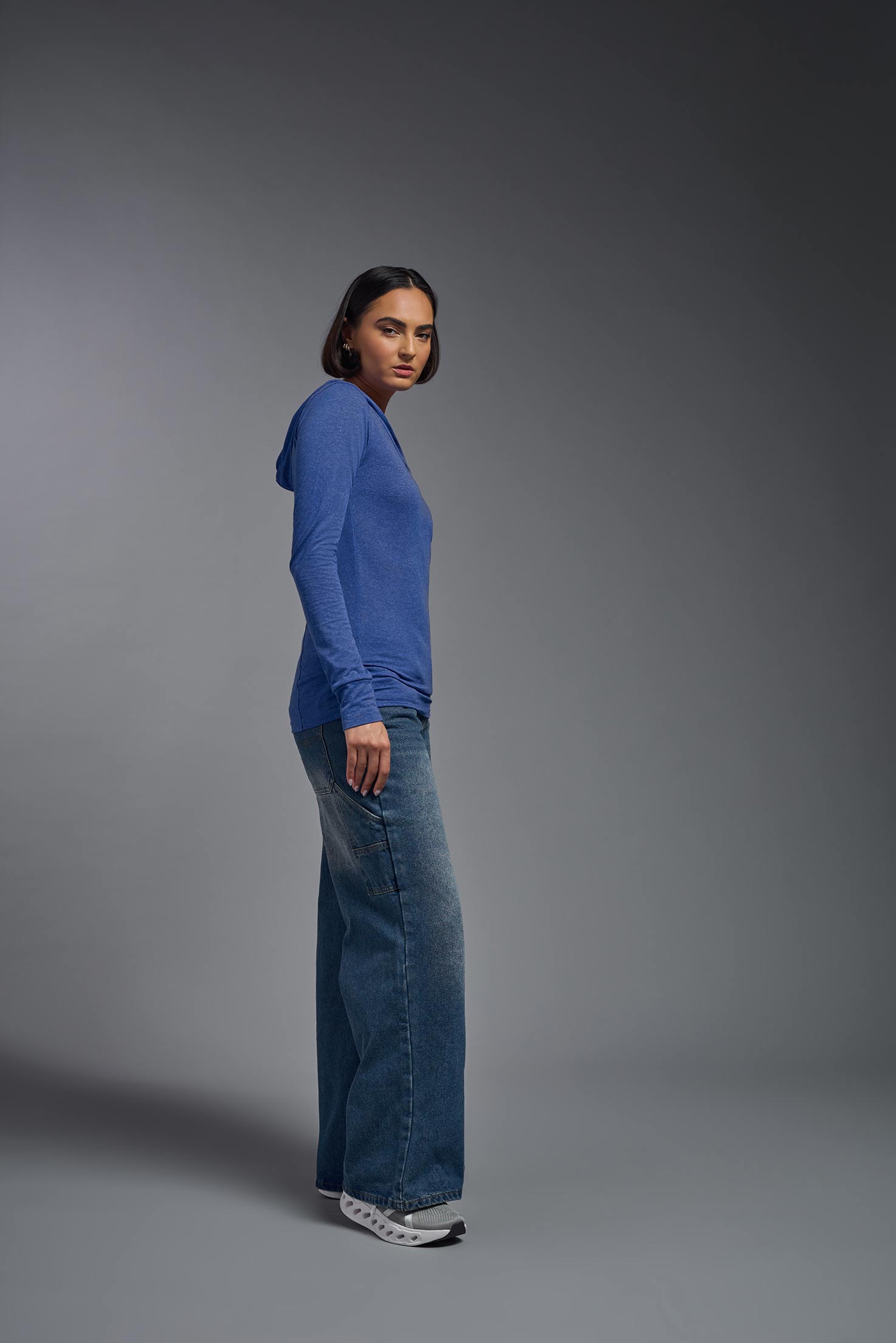 A female model wearing the women's Heather Hoodie Shirt in the color dark heather royal blue, made out of 88% polyester and 22% treated cotton, showing the relaxed fit from a side view. This hoodie shirt is comfortable and made in the USA. #dark-heather-royal