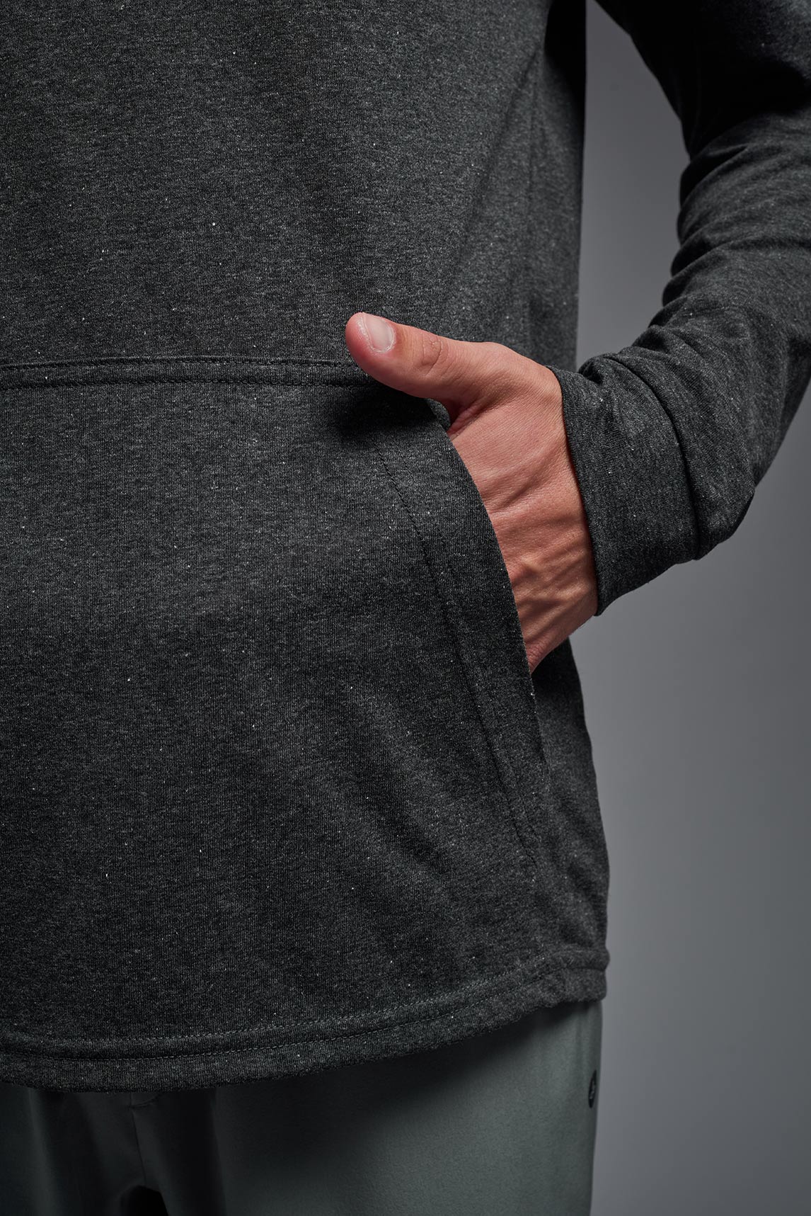 A male model wearing the men's Heather Hoodie Shirt in the color dark heather charcoal, made out of 88% polyester and 22% treated cotton, showing the relaxed fit from a closeup front pocket view. This hoodie shirt is comfortable and made in the USA. #color_dark-heather-charcoal