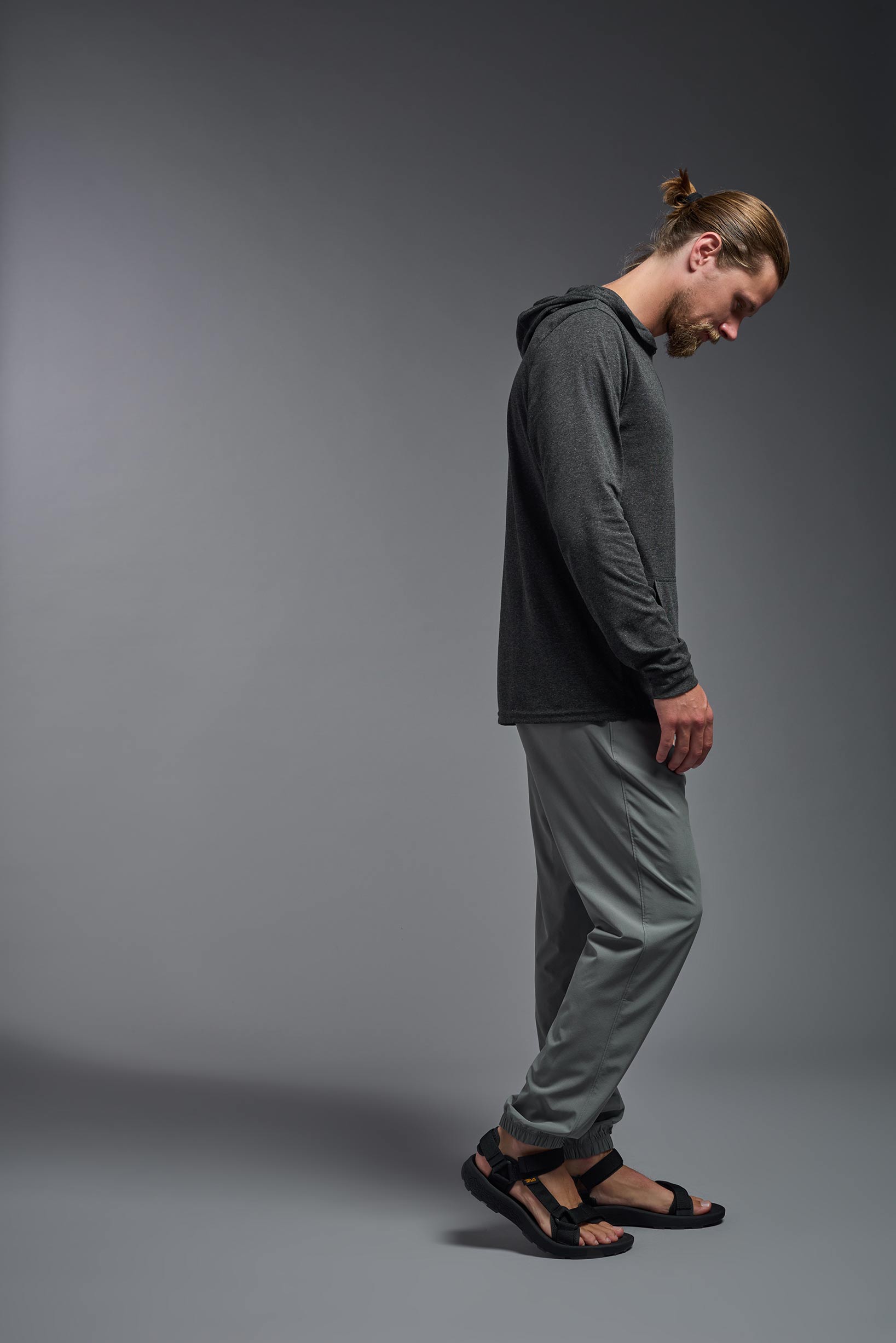 A male model wearing the men's Heather Hoodie Shirt in the color dark heather charcoal, made out of 88% polyester and 22% treated cotton, showing the relaxed fit from a side view. This hoodie shirt is comfortable and made in the USA. #color_dark-heather-charcoal