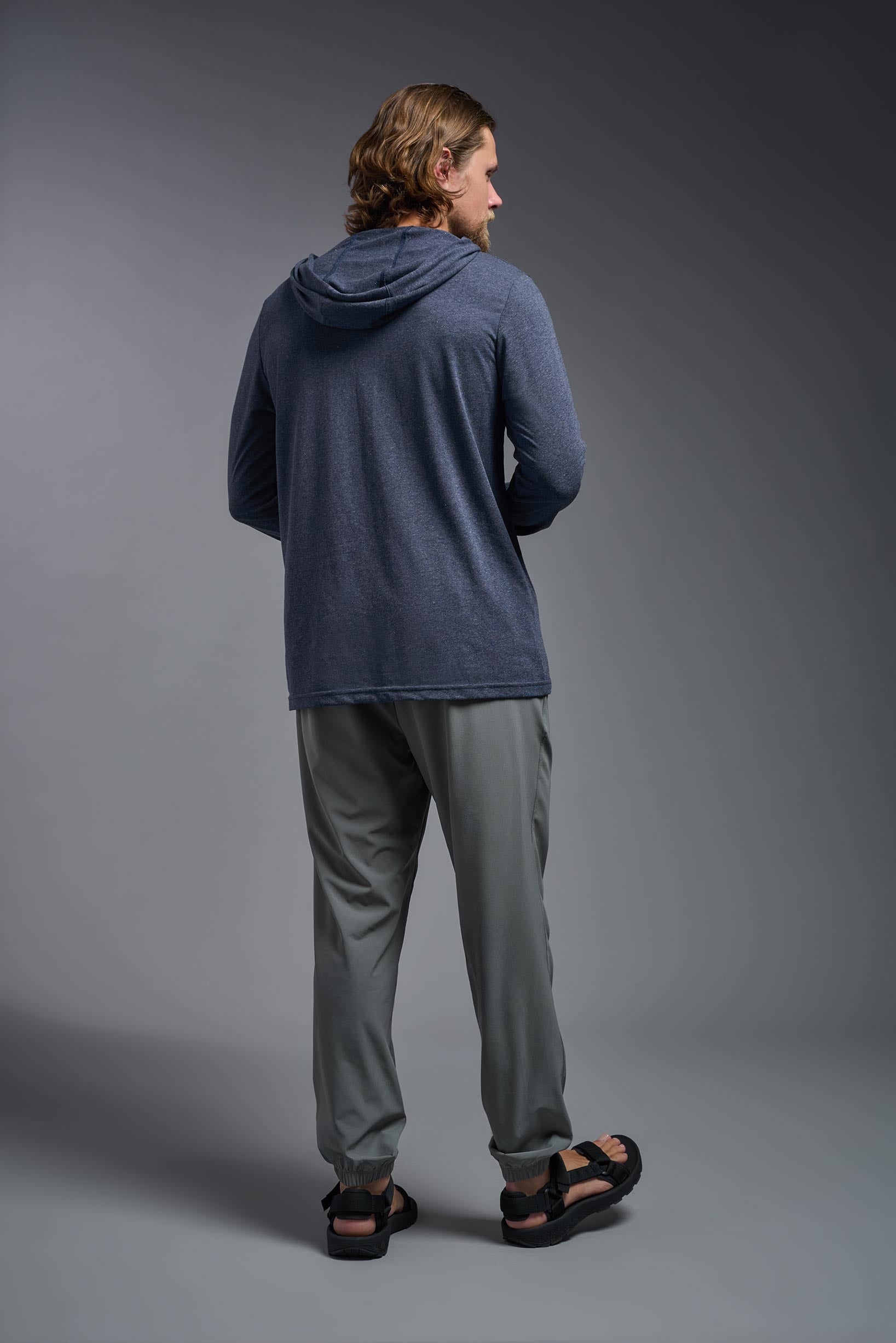 A male model wearing the men's Heather Hoodie Shirt in the color dark heather navy, made out of 88% polyester and 22% treated cotton, showing the relaxed fit from a back view. This hoodie shirt is comfortable and made in the USA. #color_dark-heather-navy