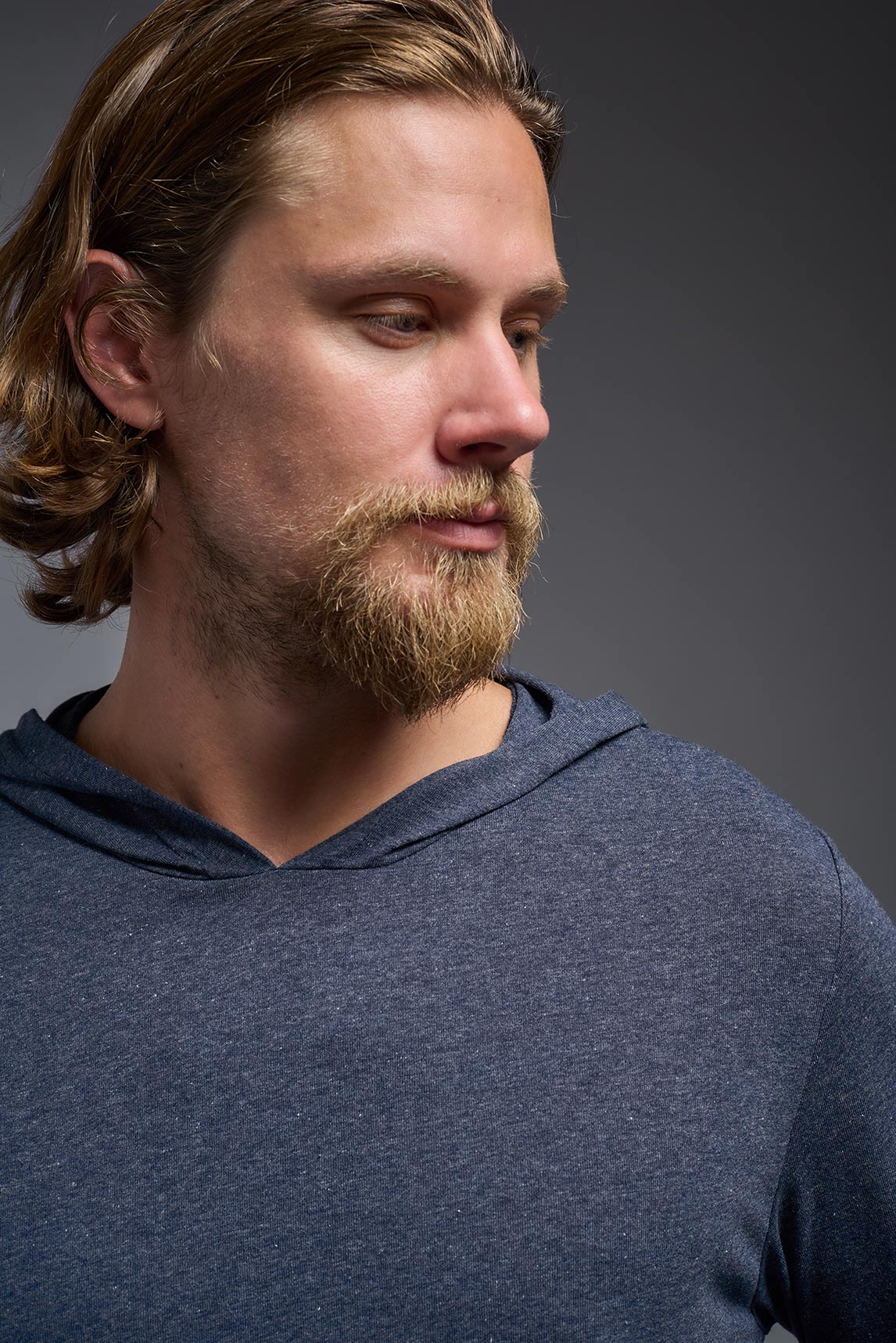 A male model wearing the men's Heather Hoodie Shirt in the color dark heather navy, made out of 88% polyester and 22% treated cotton, showing the relaxed fit from a closeup front collar view. This hoodie shirt is comfortable and made in the USA. #color_dark-heather-navy