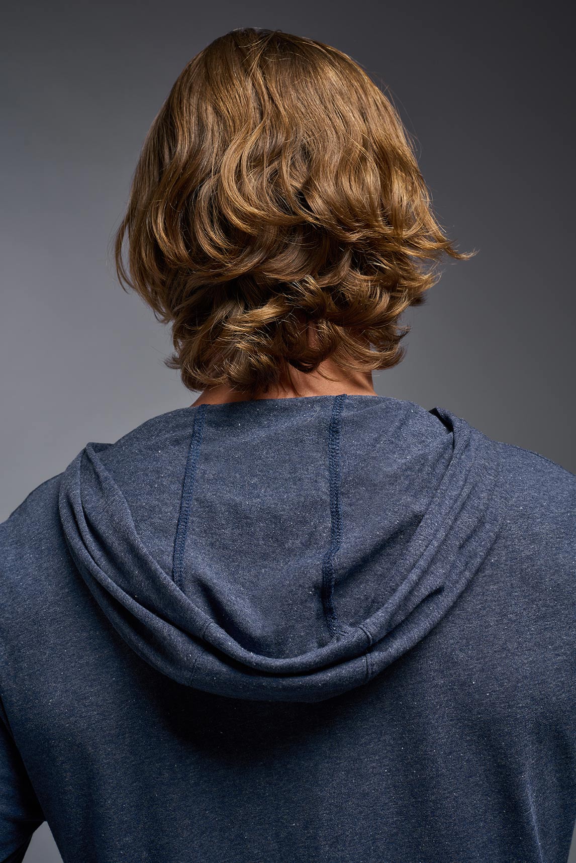 A male model wearing the men's Heather Hoodie Shirt in the color dark heather navy, made out of 88% polyester and 22% treated cotton, showing the relaxed fit from a closeup back hoodie view. This hoodie shirt is comfortable and made in the USA. #color_dark-heather-navy