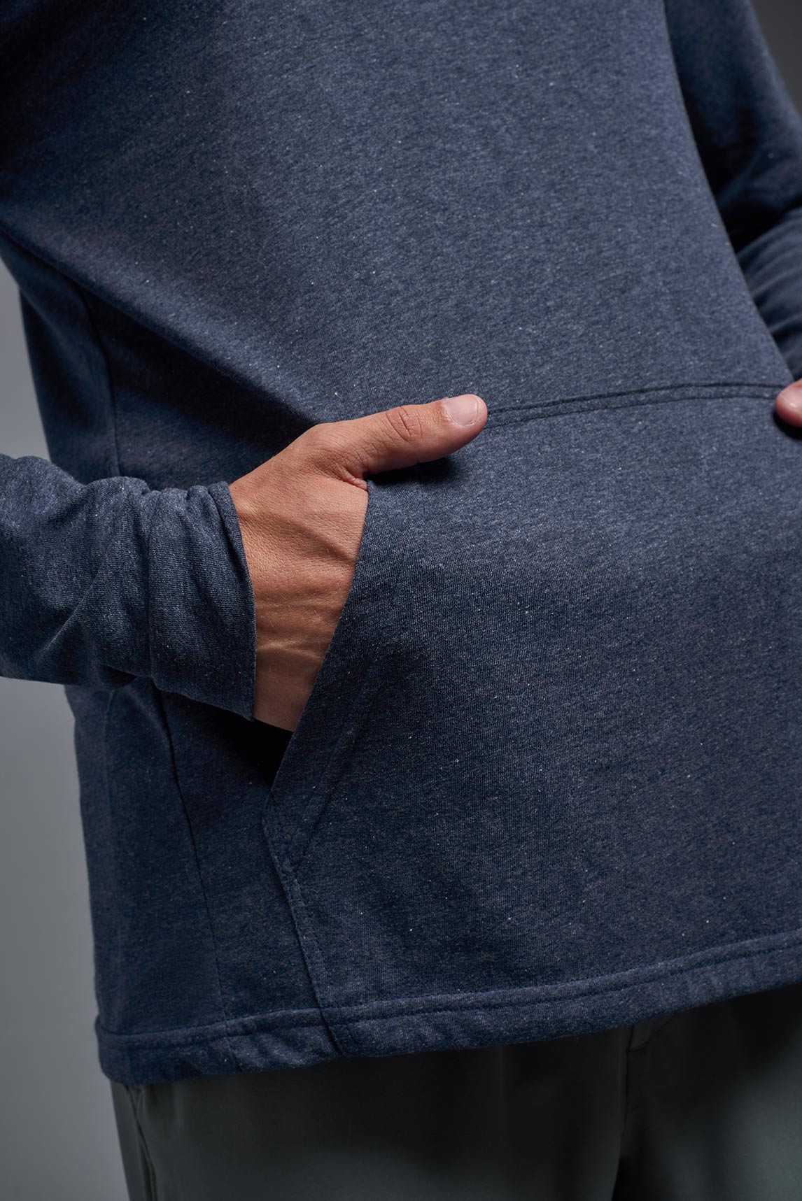 A male model wearing the men's Heather Hoodie Shirt in the color dark heather navy, made out of 88% polyester and 22% treated cotton, showing the relaxed fit from a closeup front pocket view. This hoodie shirt is comfortable and made in the USA. #color_dark-heather-navy