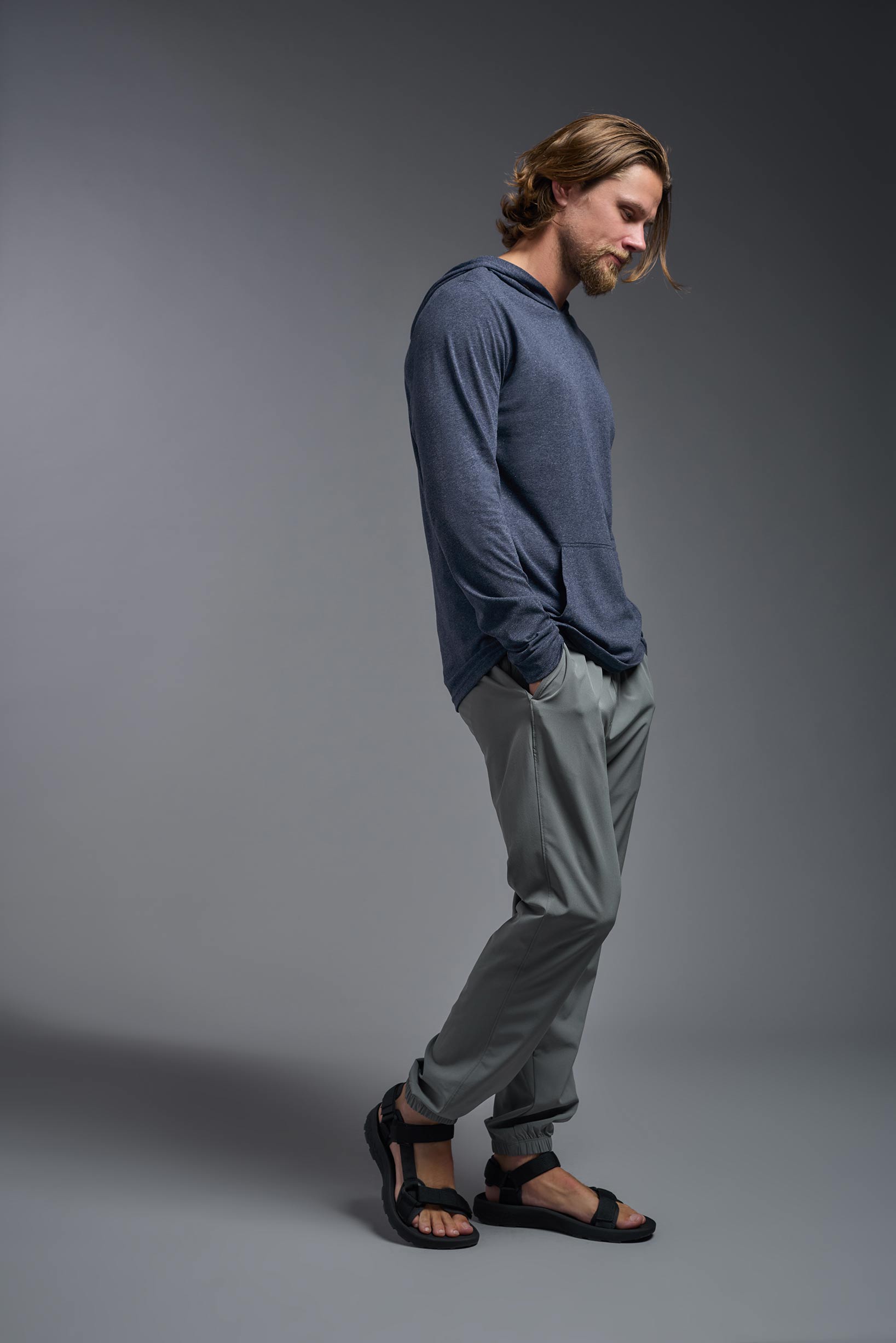 A male model wearing the men's Heather Hoodie Shirt in the color dark heather navy, made out of 88% polyester and 22% treated cotton, showing the relaxed fit from a side view. This hoodie shirt is comfortable and made in the USA. #color_dark-heather-navy