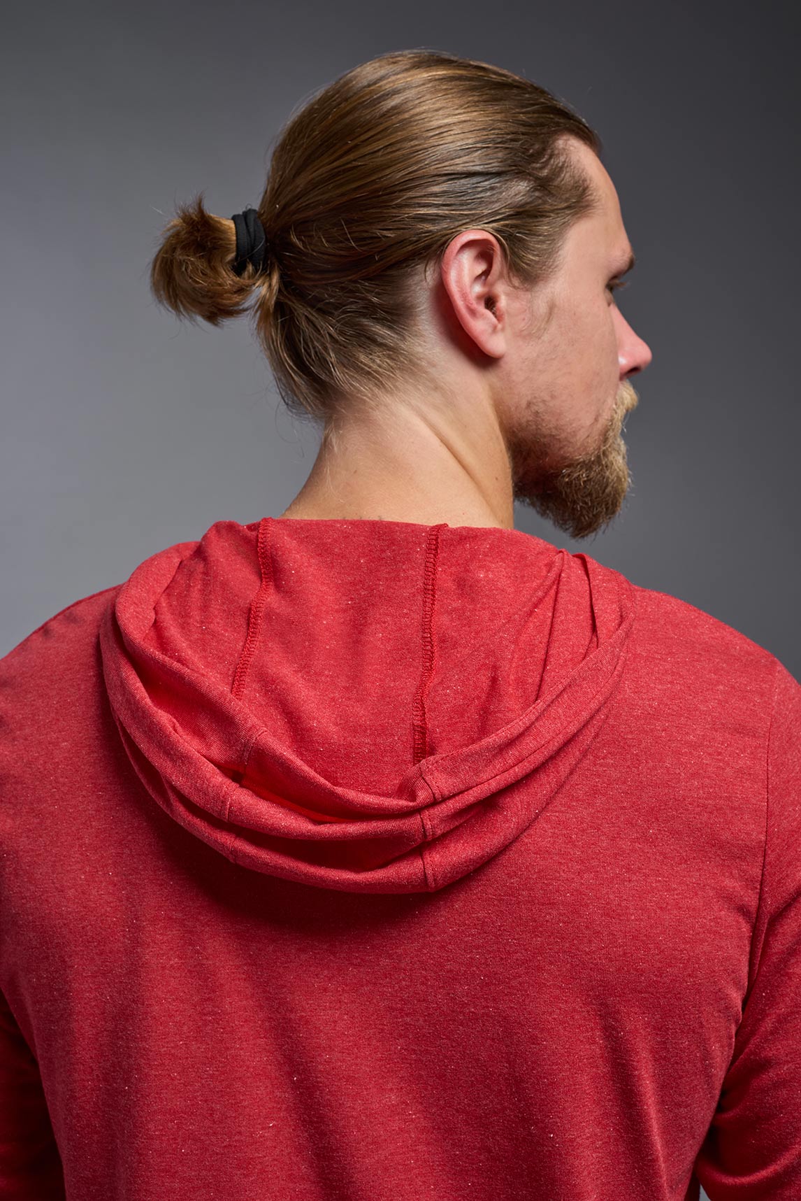 A male model wearing the men's Heather Hoodie Shirt in the color dark heather red, made out of 88% polyester and 22% treated cotton, showing the relaxed fit from a closeup back hoodie view. This hoodie shirt is comfortable and made in the USA. #color_dark-heather-red