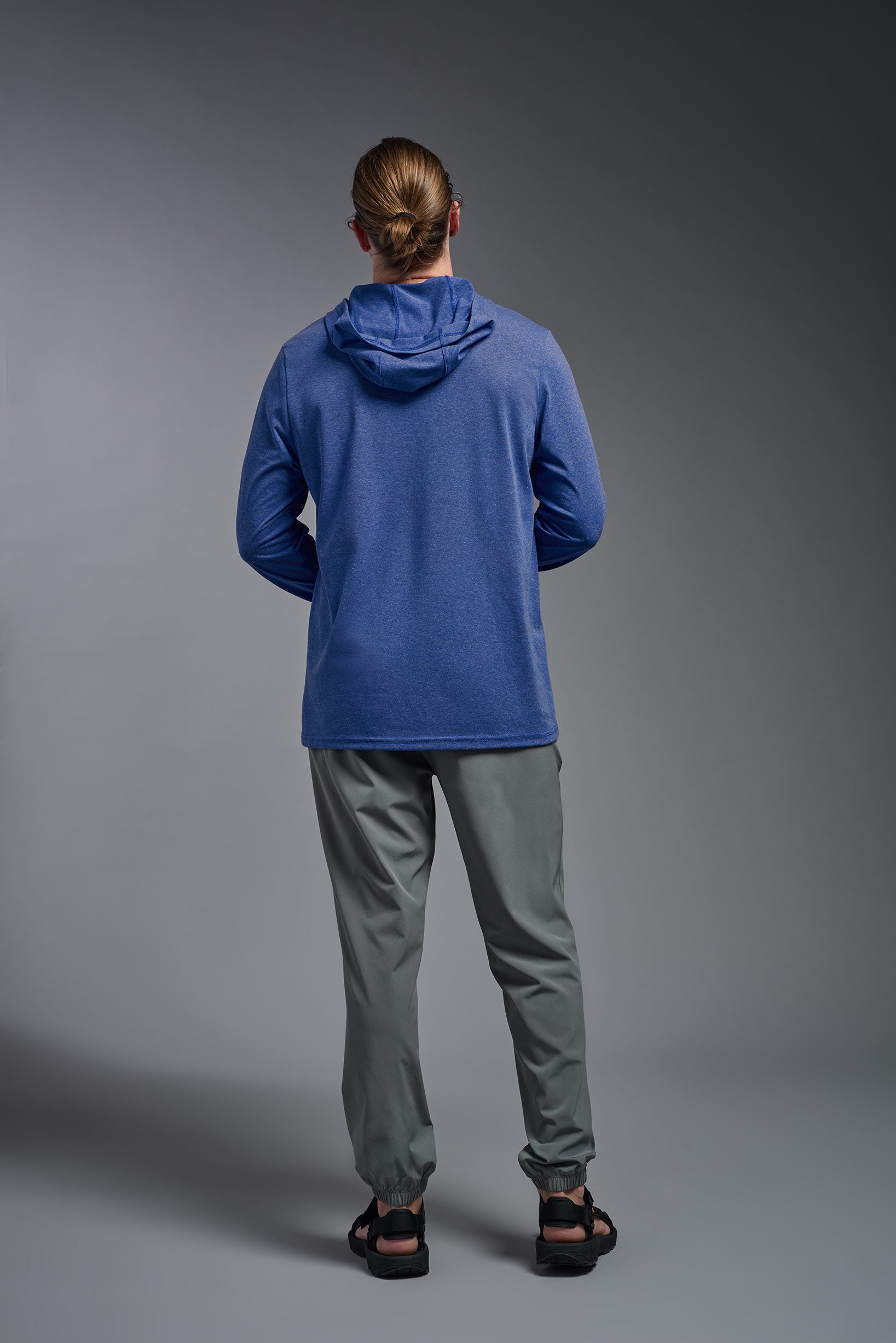 A male model wearing the men's Heather Hoodie Shirt in the color dark heather royal, made out of 88% polyester and 22% treated cotton, showing the relaxed fit from a back view. This hoodie shirt is comfortable and made in the USA. #color_dark-heather-royal