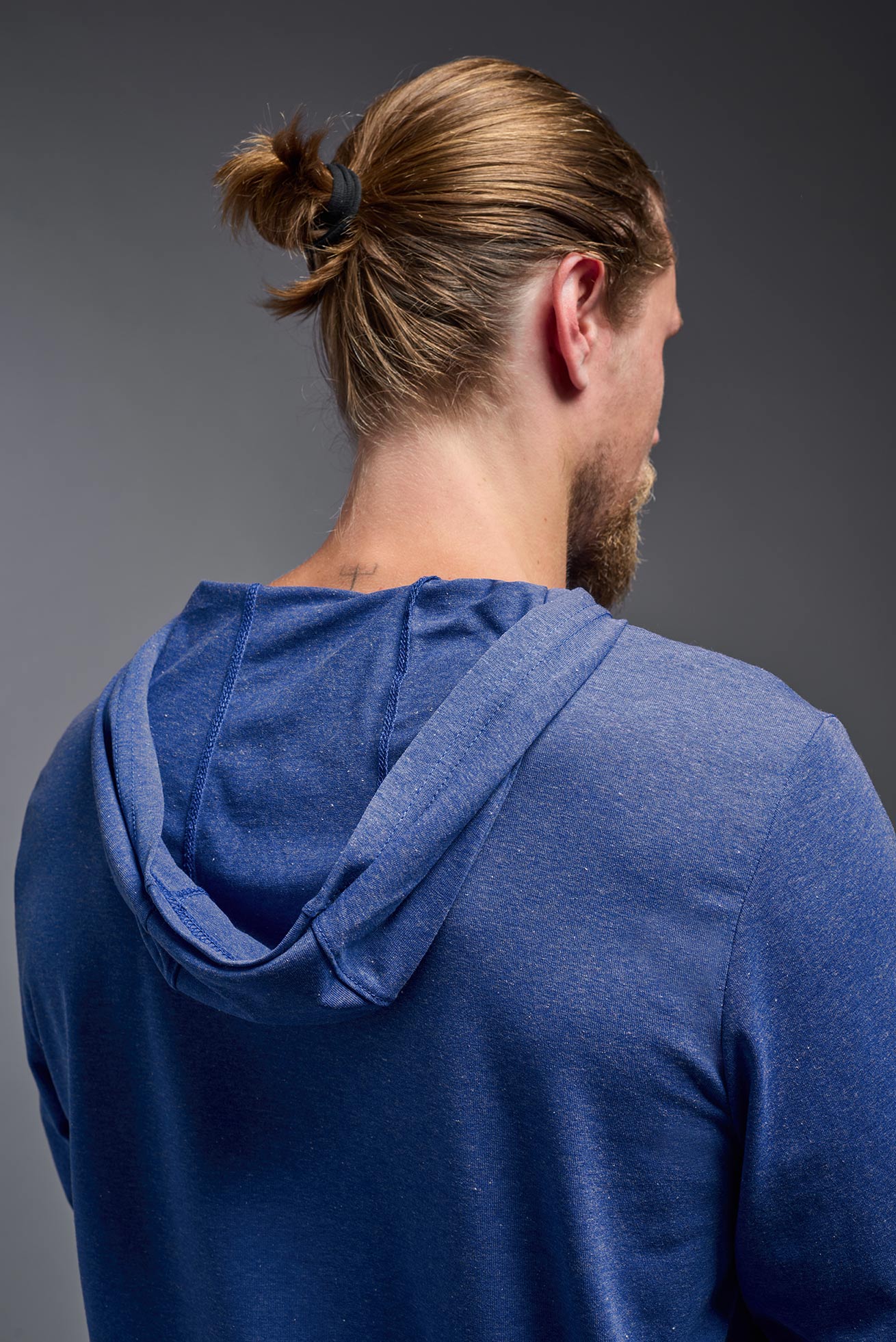 A male model wearing the men's Heather Hoodie Shirt in the color dark heather royal, made out of 88% polyester and 22% treated cotton, showing the relaxed fit from a closeup back hoodie view. This hoodie shirt is comfortable and made in the USA. #color_dark-heather-royal