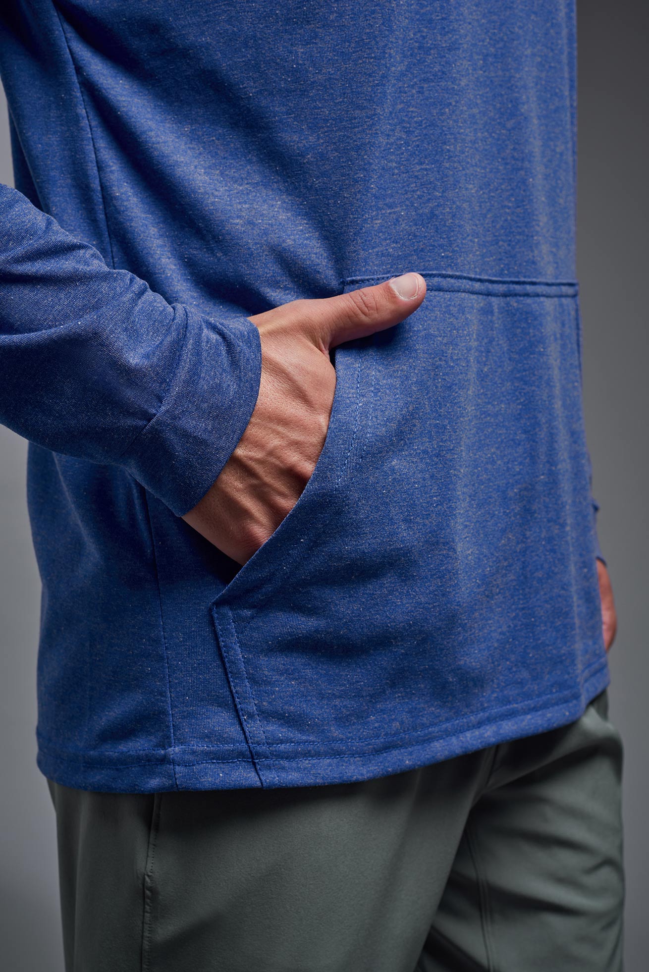 A male model wearing the men's Heather Hoodie Shirt in the color dark heather royal, made out of 88% polyester and 22% treated cotton, showing the relaxed fit from a closeup pocket view. This hoodie shirt is comfortable and made in the USA. #color_dark-heather-royal