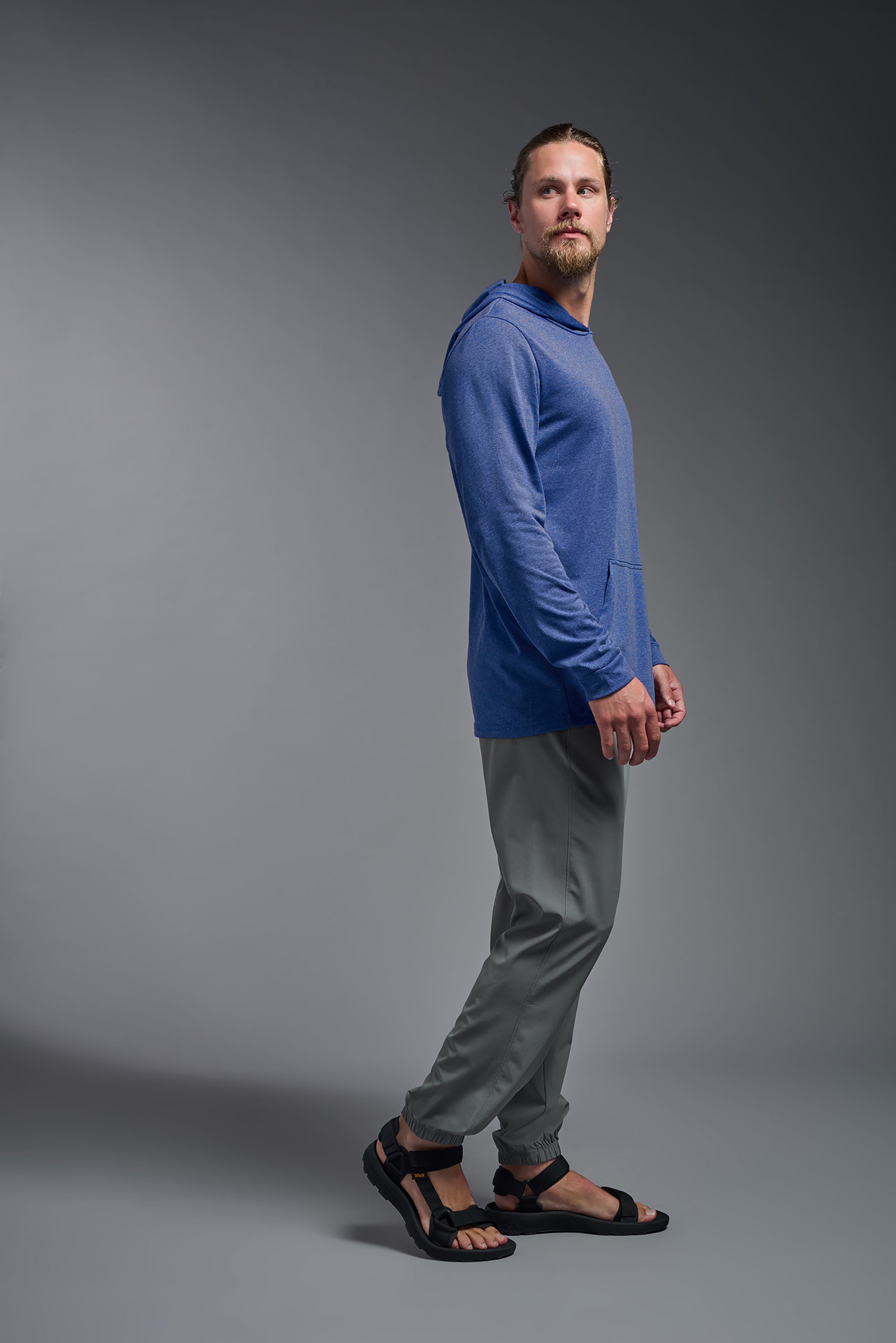 A male model wearing the men's Heather Hoodie Shirt in the color dark heather royal, made out of 88% polyester and 22% treated cotton, showing the relaxed fit from a side view. This hoodie shirt is comfortable and made in the USA. #color_dark-heather-royal