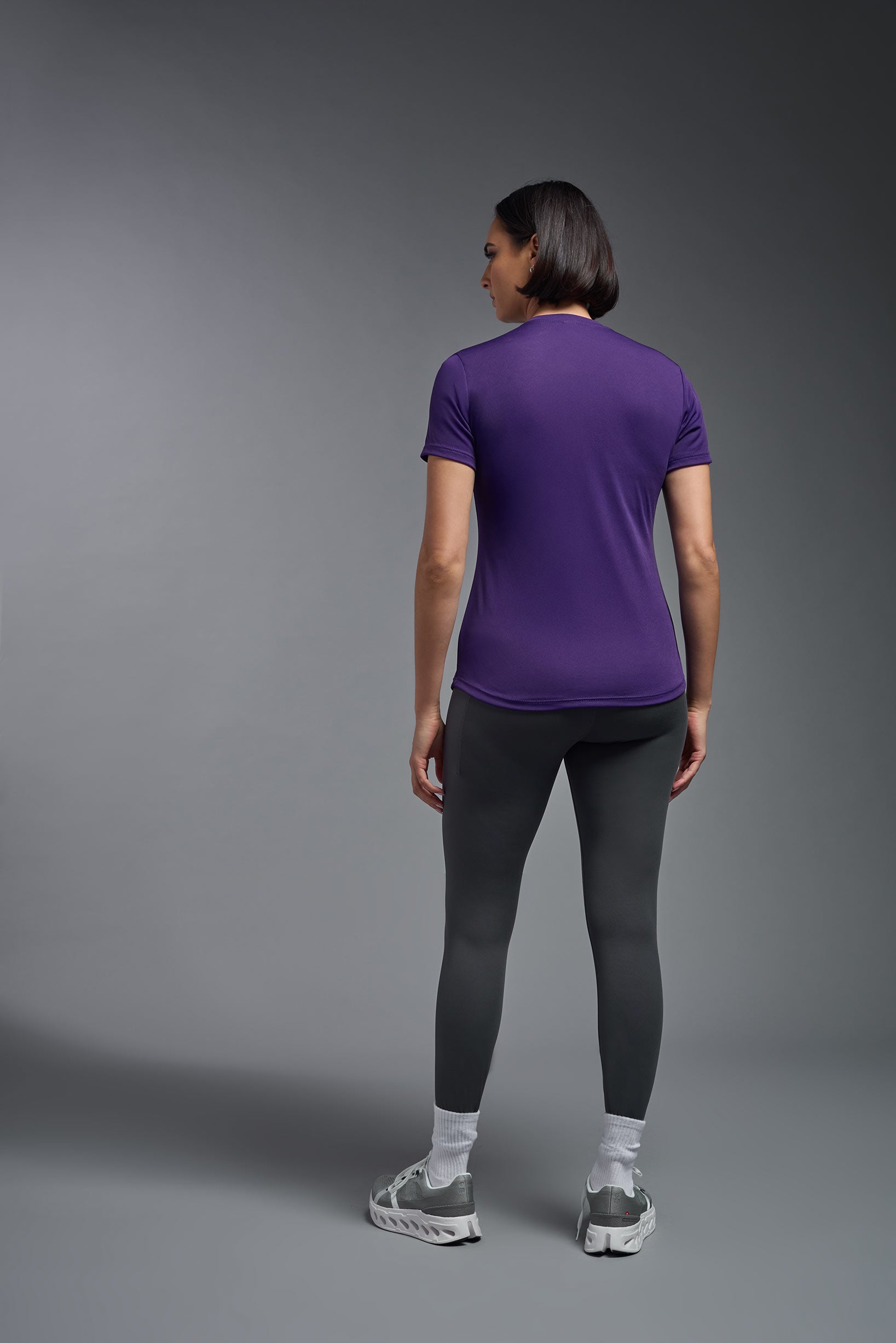 A female model wearing the women's DriMax Crewneck Expert Tee in the color dark purple, made out of 100% polyester, showing the relaxed fit from a back view. This shirt is quick-drying, moisture-wicking, offers up to 30 upf protection and is made in the USA. #deep-purple