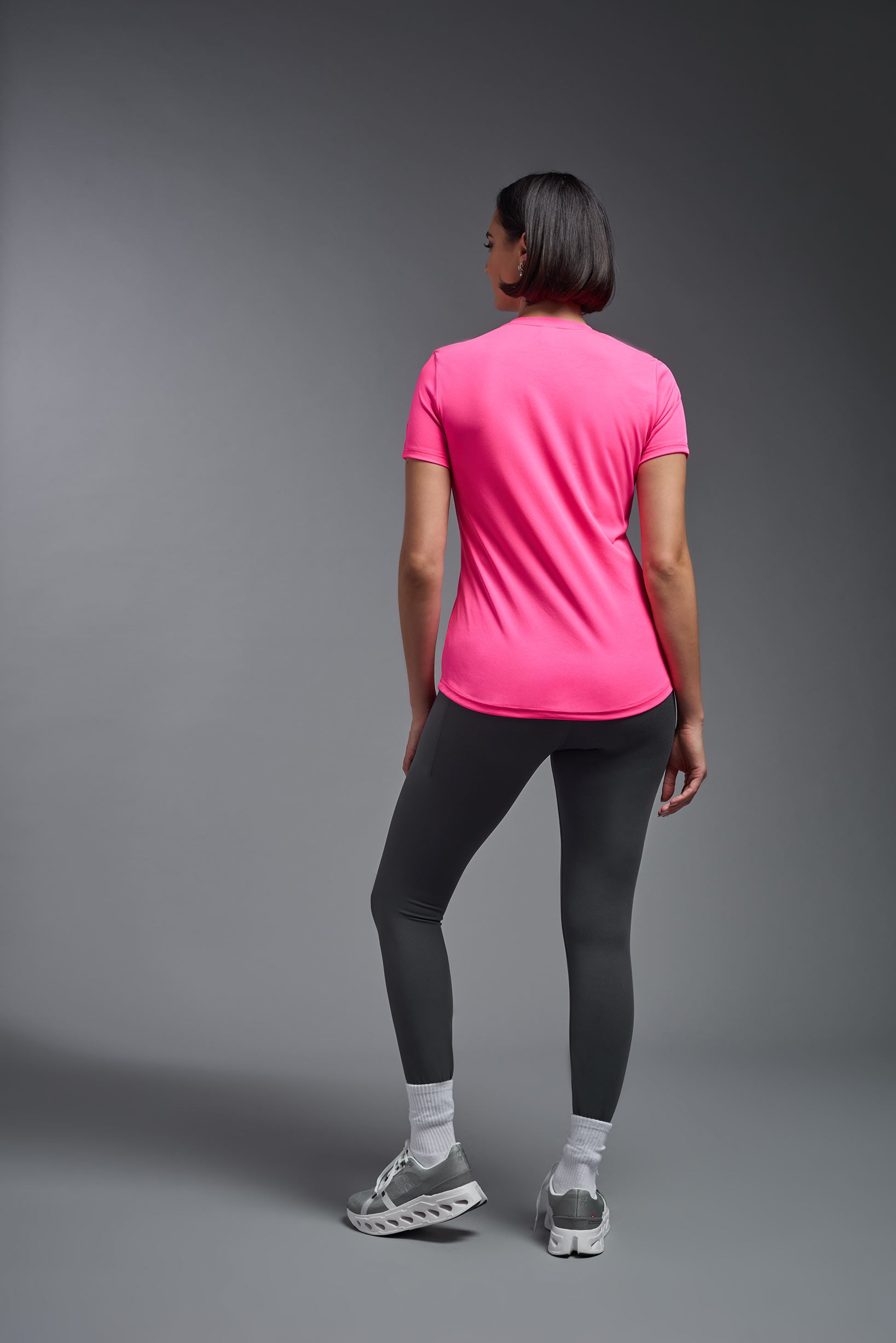 A female model wearing the women's DriMax Crewneck Expert Tee in the color hot pink, made out of 100% polyester, showing the relaxed fit from a back view. This shirt is quick-drying, moisture-wicking, offers up to 30 upf protection and is made in the USA. #hot-pink