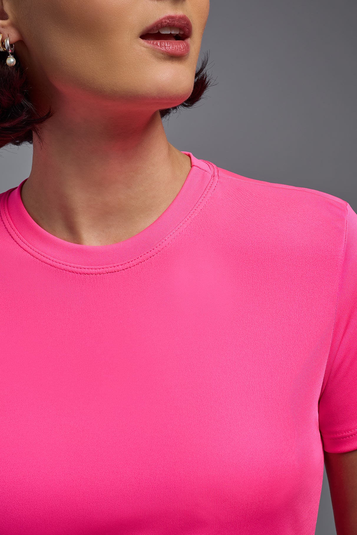 A female model wearing the women's DriMax Crewneck Expert Tee in the color hot pink, made out of 100% polyester, showing the relaxed fit from a close-up collar view. This shirt is quick-drying, moisture-wicking, offers up to 30 upf protection and is made in the USA. #hot-pink