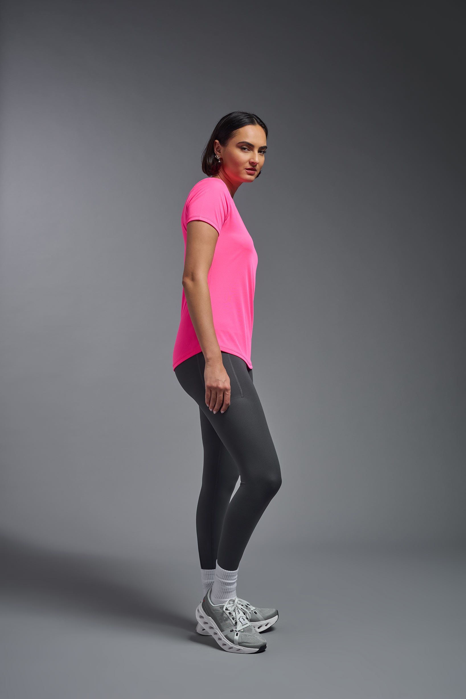 A female model wearing the women's DriMax Crewneck Expert Tee in the color hot pink, made out of 100% polyester, showing the relaxed fit from a side view. This shirt is quick-drying, moisture-wicking, offers up to 30 upf protection and is made in the USA. #hot-pink