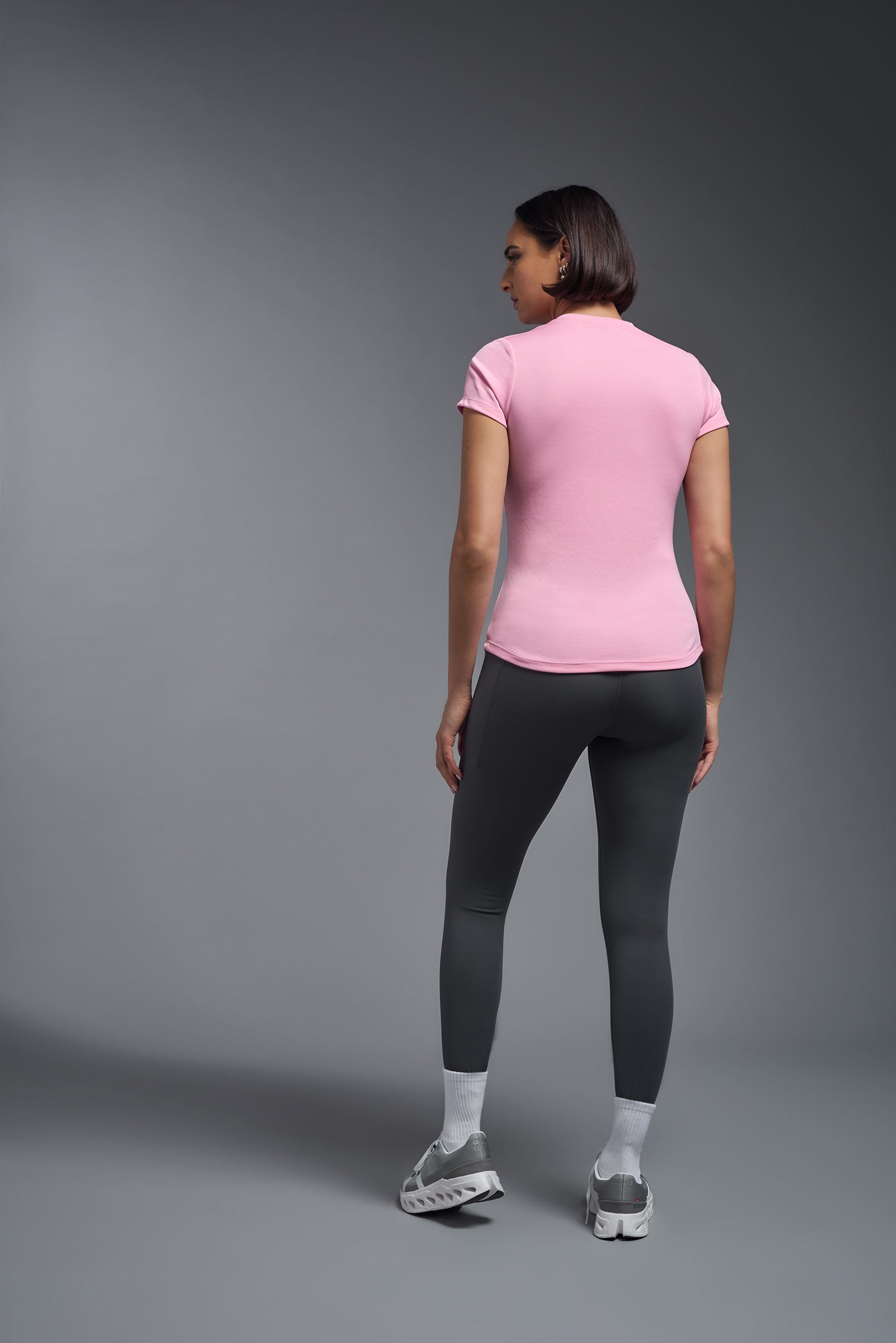 A female model wearing the women's DriMax Crewneck Expert Tee in the color pink, made out of 100% polyester, showing the relaxed fit from a back view. This shirt is quick-drying, moisture-wicking, offers up to 30 upf protection and is made in the USA. #pink