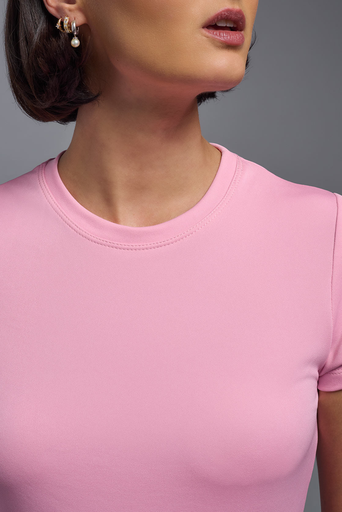 A female model wearing the women's DriMax Crewneck Expert Tee in the color pink, made out of 100% polyester, showing the relaxed fit from a close-up collar view. This shirt is quick-drying, moisture-wicking, offers up to 30 upf protection and is made in the USA. #pink