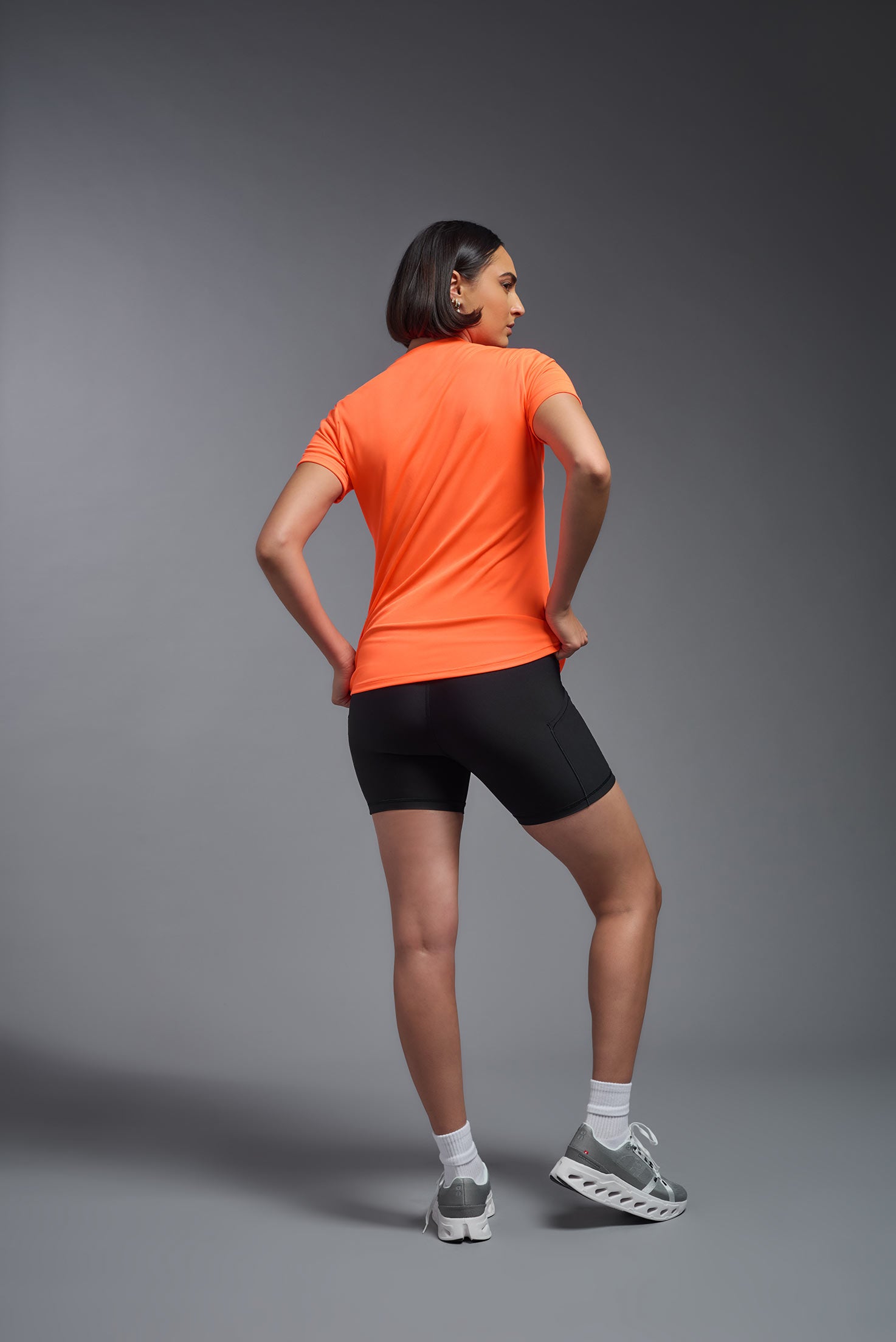 A female model wearing the women's DriMax Crewneck Expert Tee in the color safety orange made out of 100% polyester, showing the relaxed fit from a back view. This shirt is quick-drying, moisture-wicking, offers up to 30 upf protection and is made in the USA. #safety-orange
