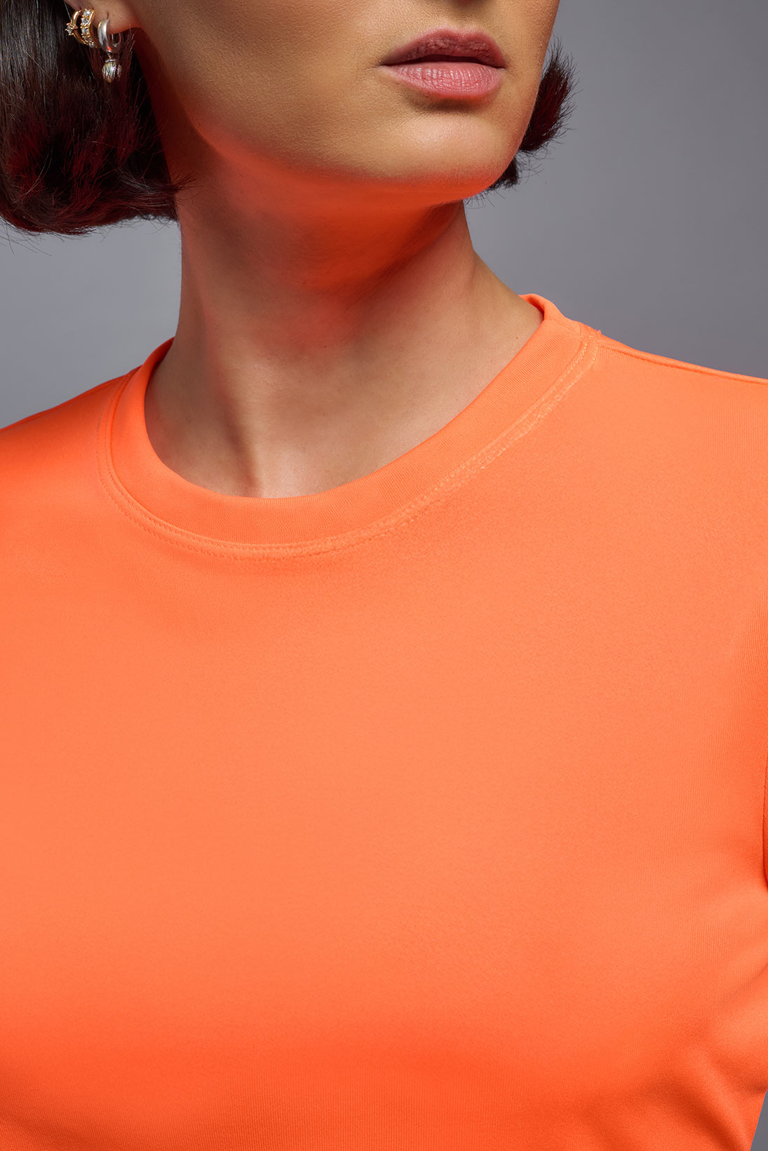 A female model wearing the women's DriMax Crewneck Expert Tee in the color safety orange made out of 100% polyester, showing the relaxed fit from a collar close-up view. This shirt is quick-drying, moisture-wicking, offers up to 30 upf protection and is made in the USA. #safety-orange