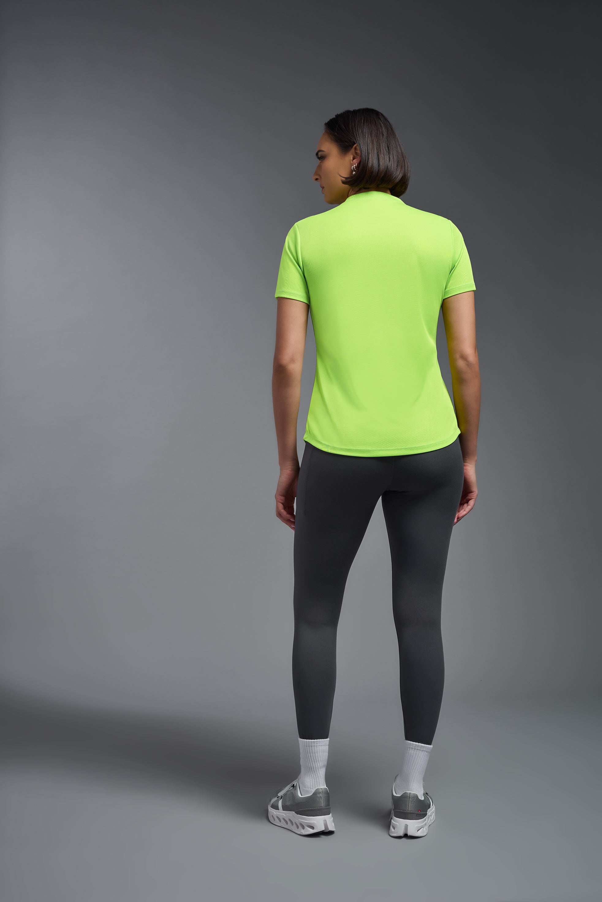 A female model wearing the women's DriMax Crewneck Expert Tee in the color safety yellow made out of 100% polyester, showing the relaxed fit from a back view. This shirt is quick-drying, moisture-wicking, offers up to 30 upf protection and is made in the USA. #safety-yellow