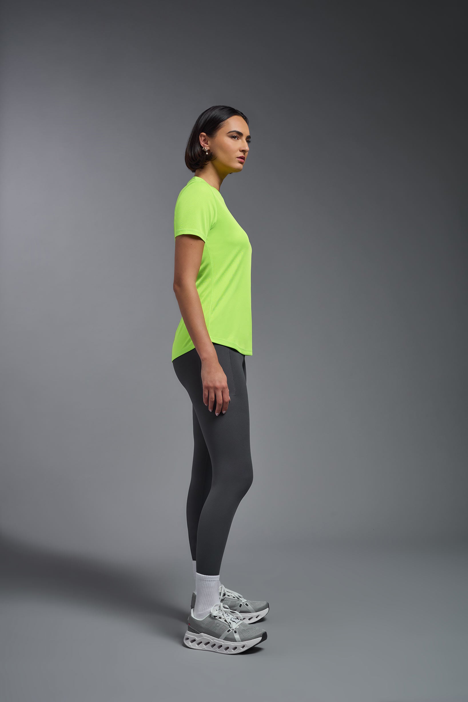 A female model wearing the women's DriMax Crewneck Expert Tee in the color safety yellow made out of 100% polyester, showing the relaxed fit from a side view. This shirt is quick-drying, moisture-wicking, offers up to 30 upf protection and is made in the USA. #safety-yellow