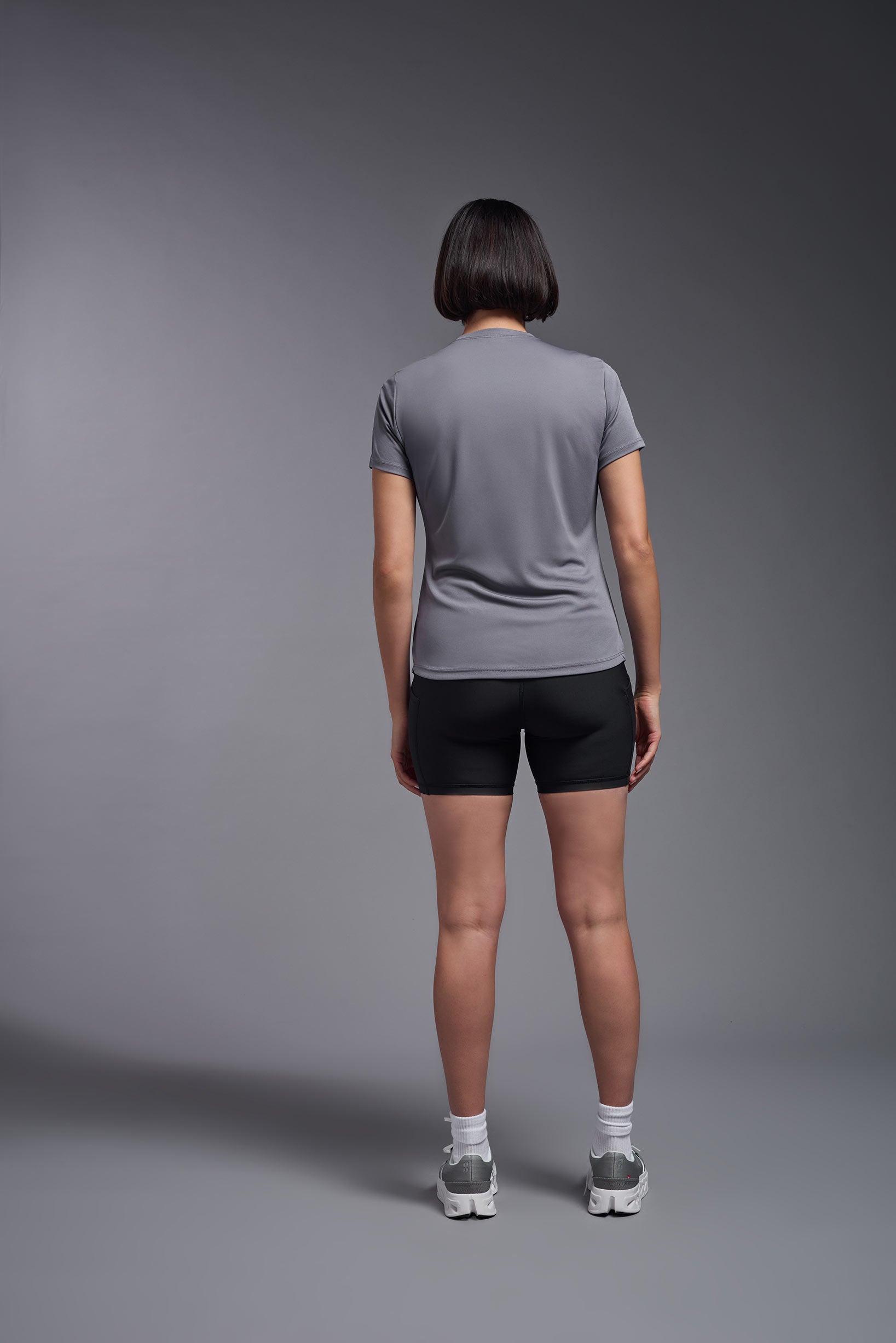A female model wearing the women's DriMax Crewneck Expert Tee in the color steel gray made out of 100% polyester, showing the relaxed fit from a back view. This shirt is quick-drying, moisture-wicking, offers up to 30 upf protection and is made in the USA. #steel