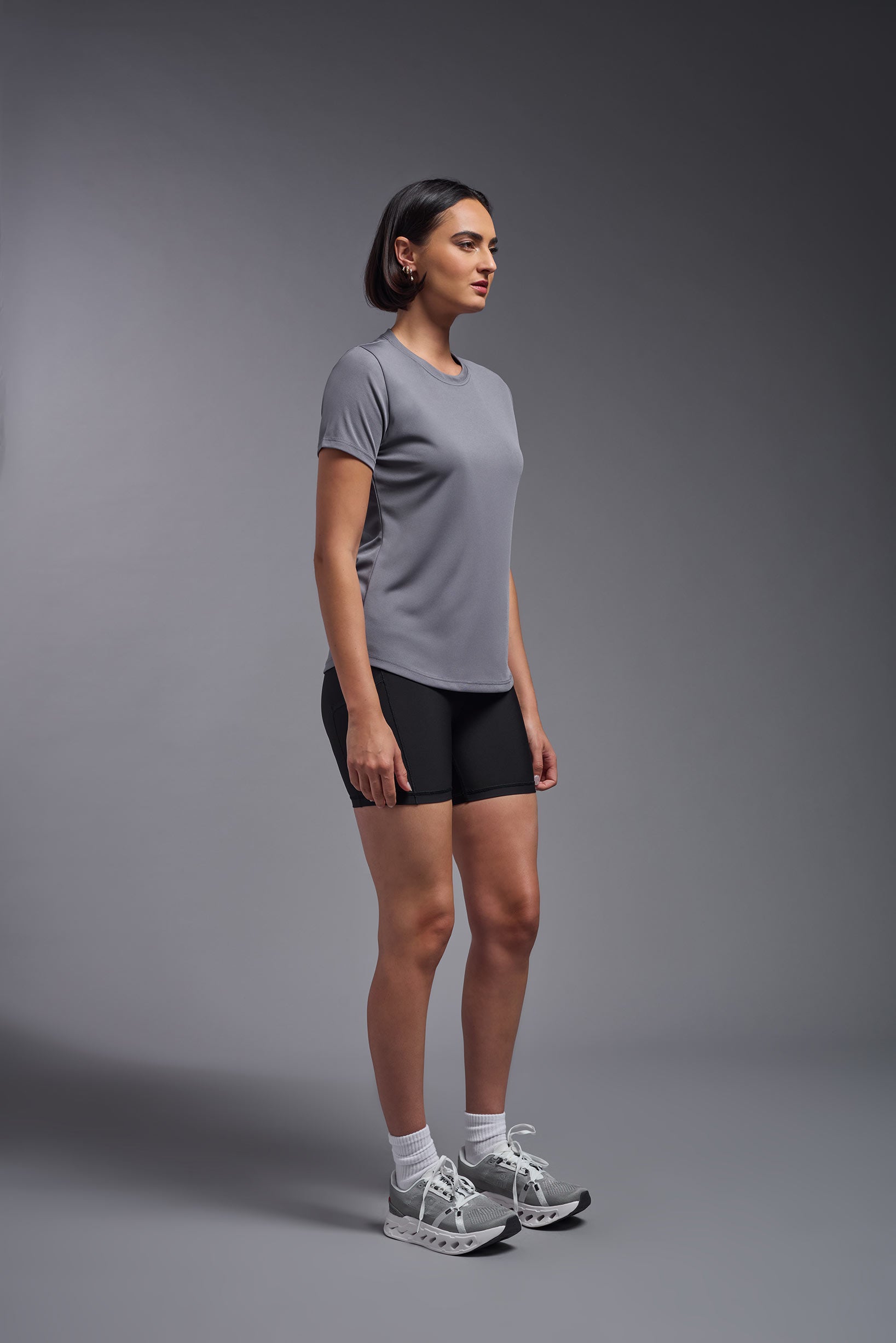A female model wearing the women's DriMax Crewneck Expert Tee in the color steel gray made out of 100% polyester, showing the relaxed fit from a side view. This shirt is quick-drying, moisture-wicking, offers up to 30 upf protection and is made in the USA. #steel