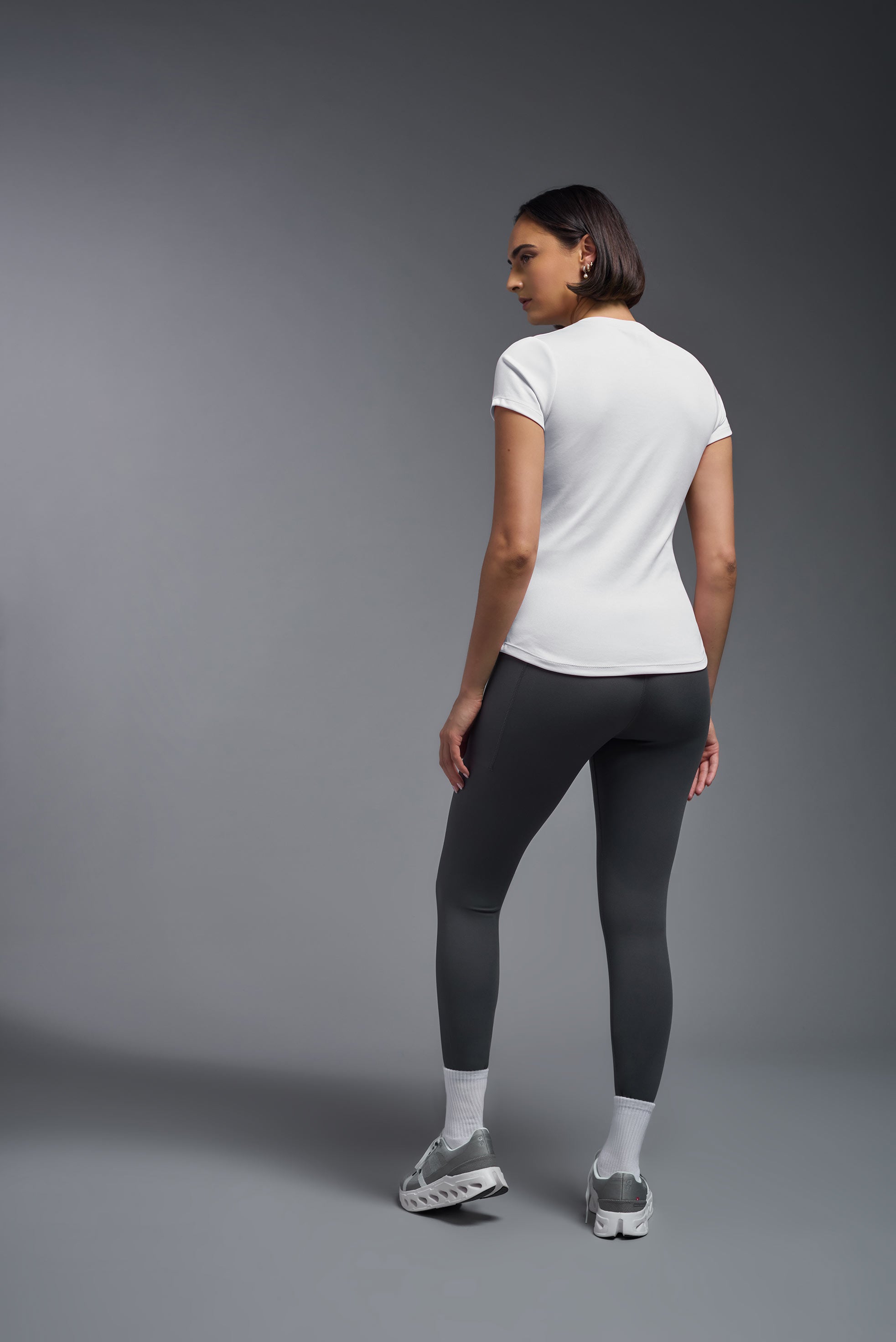 A female model wearing the women's DriMax Crewneck Expert Tee in the color white made out of 100% polyester, showing the relaxed fit from a back view. This shirt is quick-drying, moisture-wicking, offers up to 30 upf protection and is made in the USA. #white