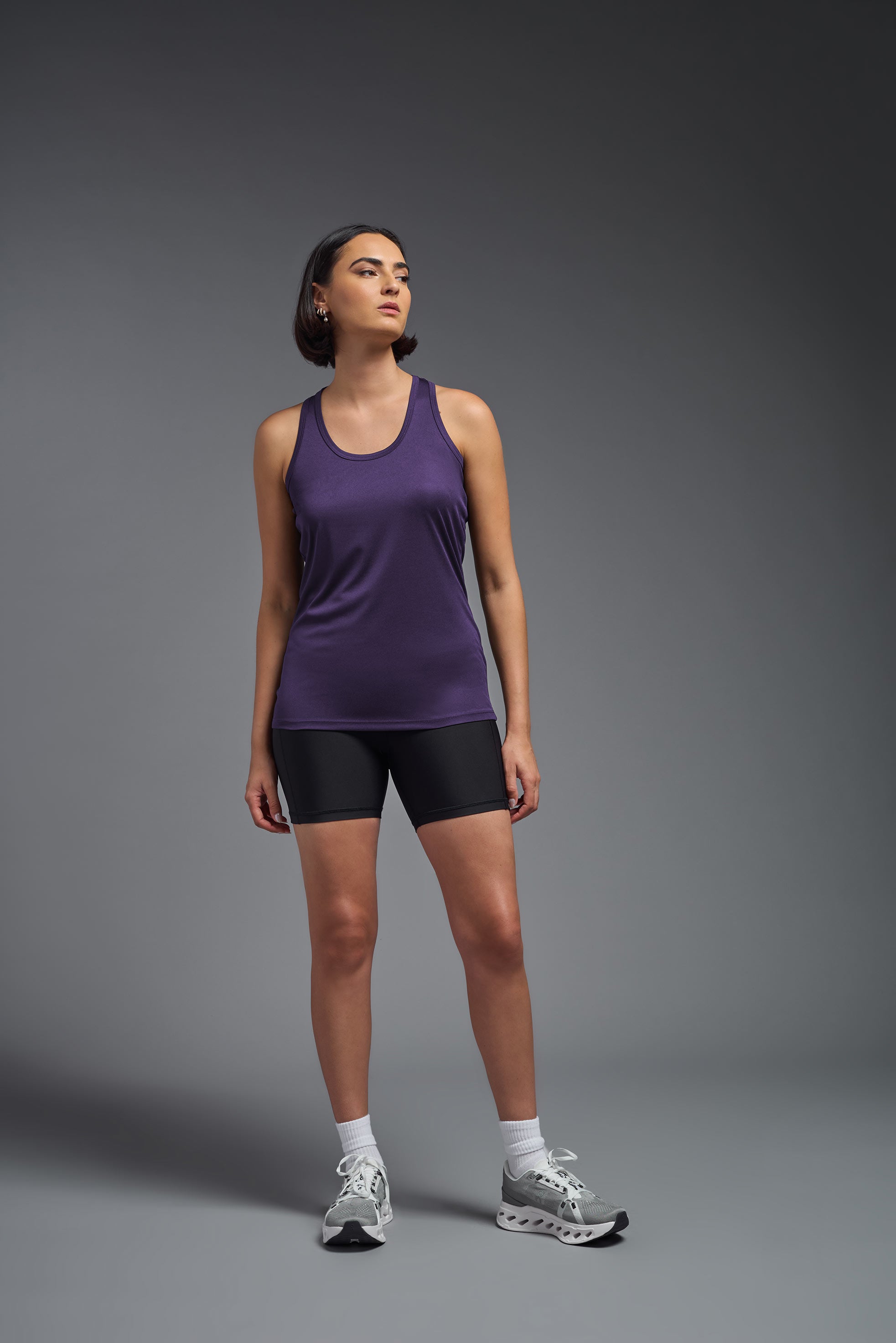A female model wearing the women's DriMax Endurance Racerback Tank in the color dark purple, made out of 100% polyester, showing the relaxed fit from a front view. This tank is quick-drying, moisture-wicking, with up to 30 UV protection and made in the USA. #dark-purple