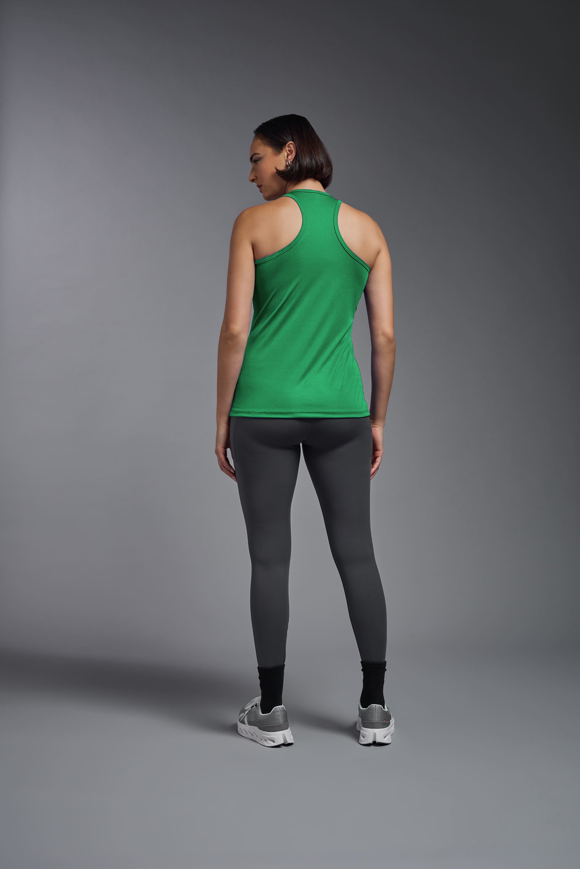 A female model wearing the women's DriMax Endurance Racerback Tank in the color kelly green, made out of 100% polyester, showing the relaxed fit from a back view. This tank is quick-drying, moisture-wicking, with up to 30 UV protection and made in the USA. #kelly-green