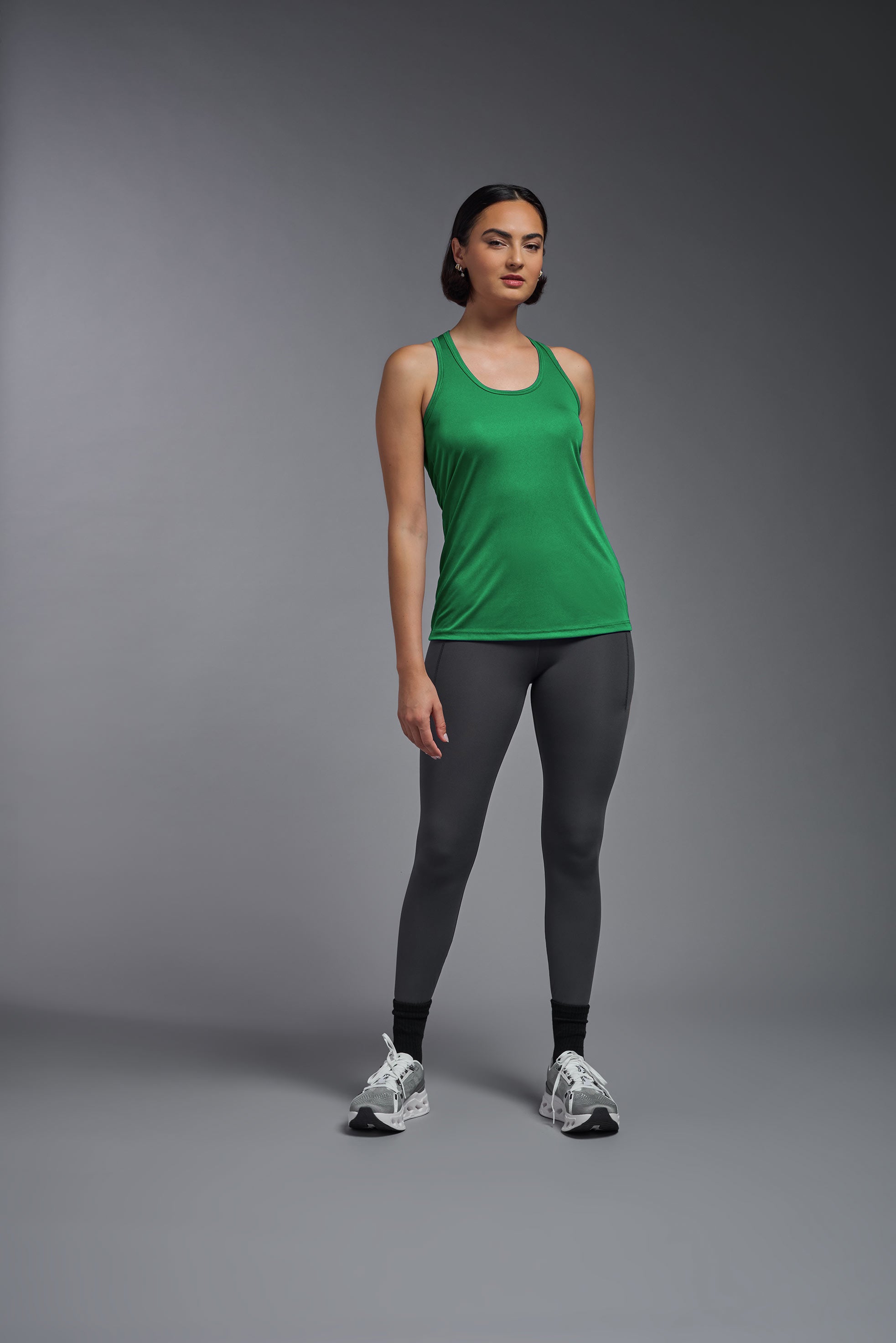 A female model wearing the women's DriMax Endurance Racerback Tank in the color kelly green, made out of 100% polyester, showing the relaxed fit from a front view. This tank is quick-drying, moisture-wicking, with up to 30 UV protection and made in the USA. #kelly-green