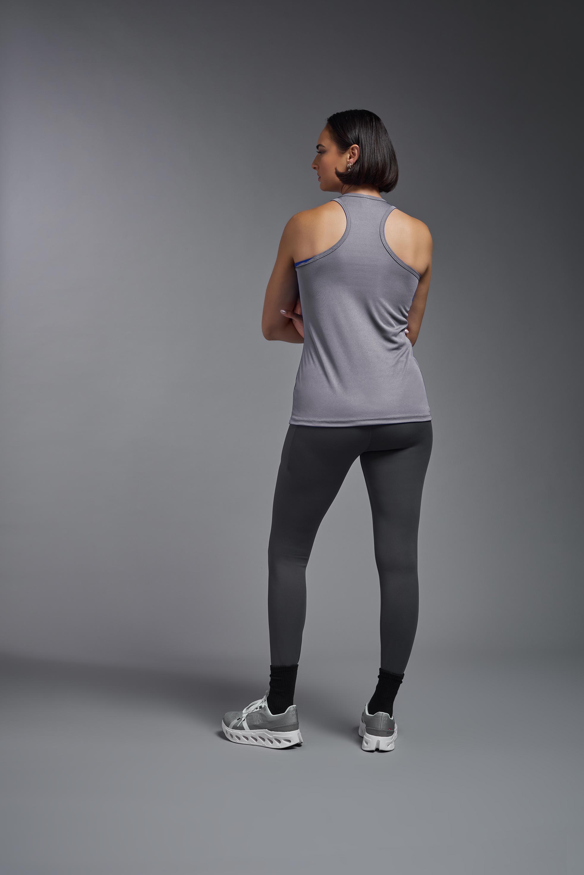 A female model wearing the women's DriMax Endurance Racerback Tank in the color steel gray, made out of 100% polyester, showing the relaxed fit from a back view. This tank is quick-drying, moisture-wicking, with up to 30 UV protection and made in the USA. #steel