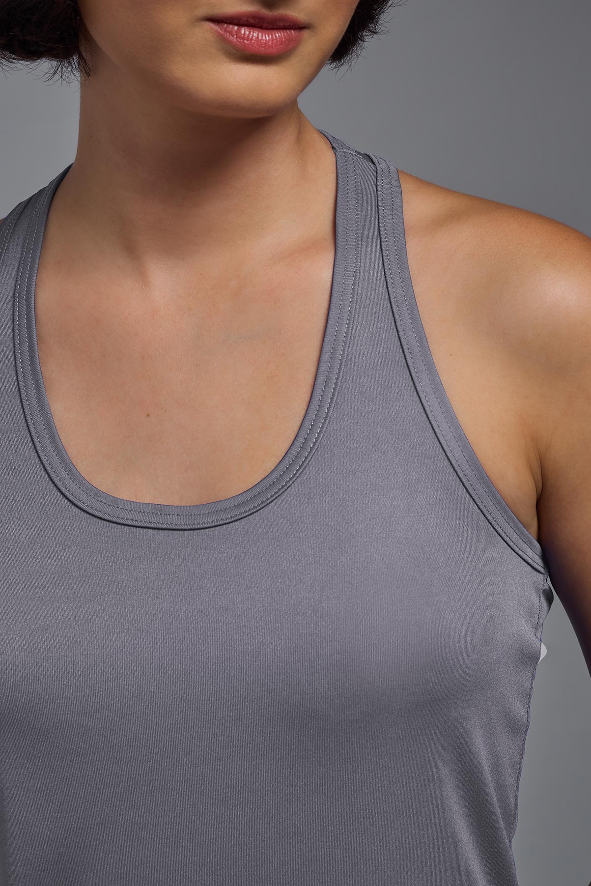 A female model wearing the women's DriMax Endurance Racerback Tank in the color steel gray, made out of 100% polyester, showing the relaxed fit from closeup collar front view. This tank is quick-drying, moisture-wicking, with up to 30 UV protection and made in the USA. #steel